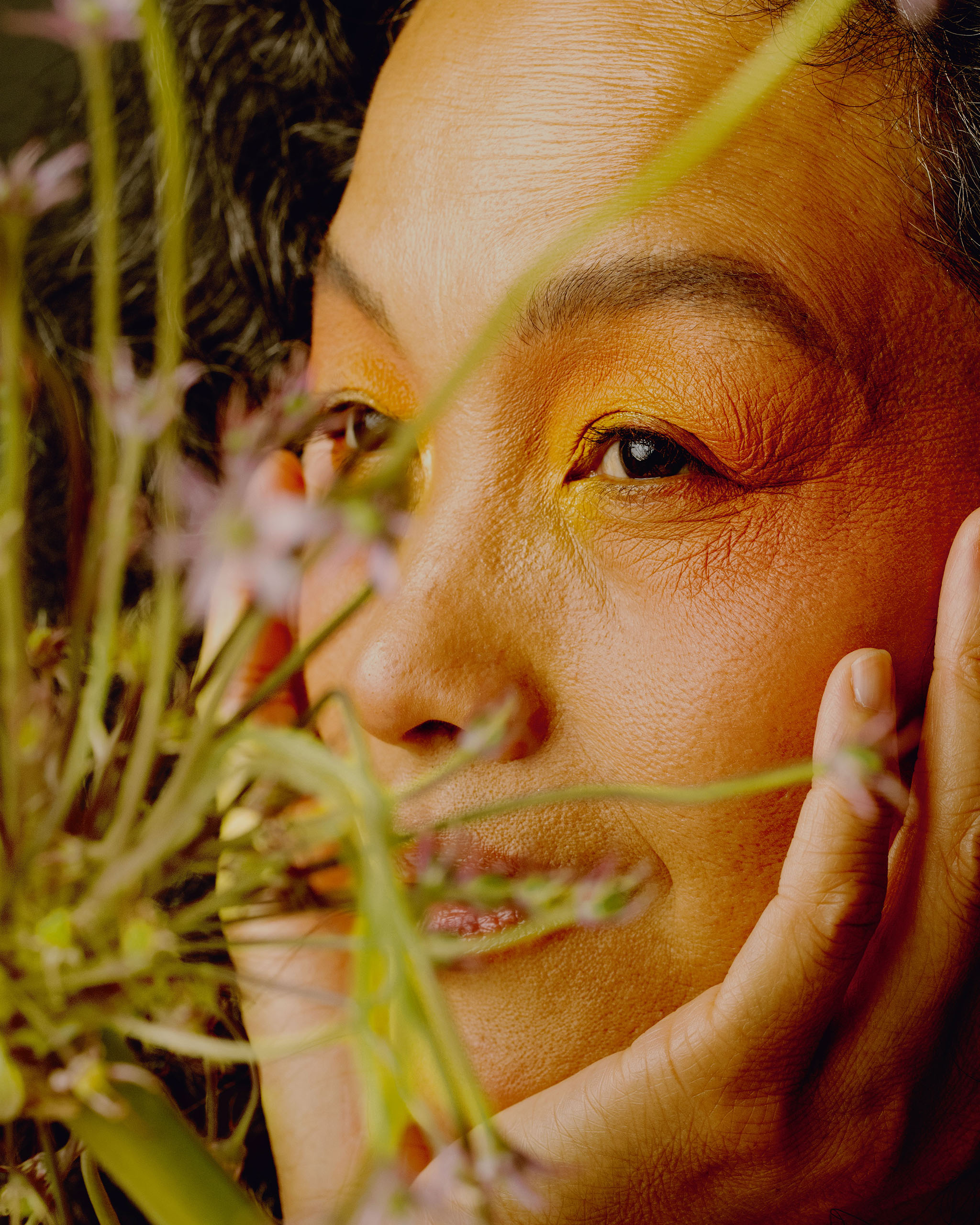 A portrait of a woman smiling with pink flowers in front of her.