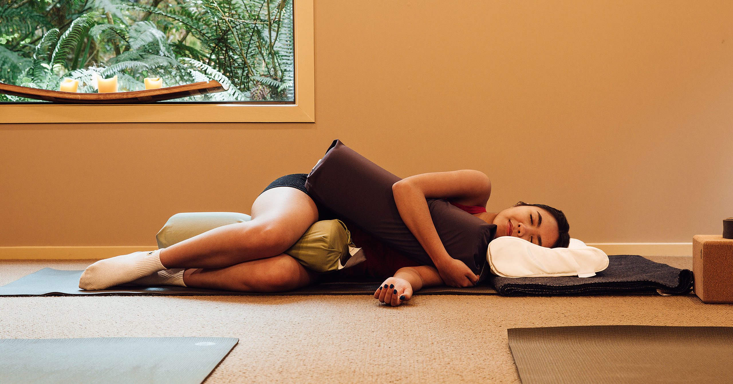 A woman laying down on a yoga mat and hugging pillows