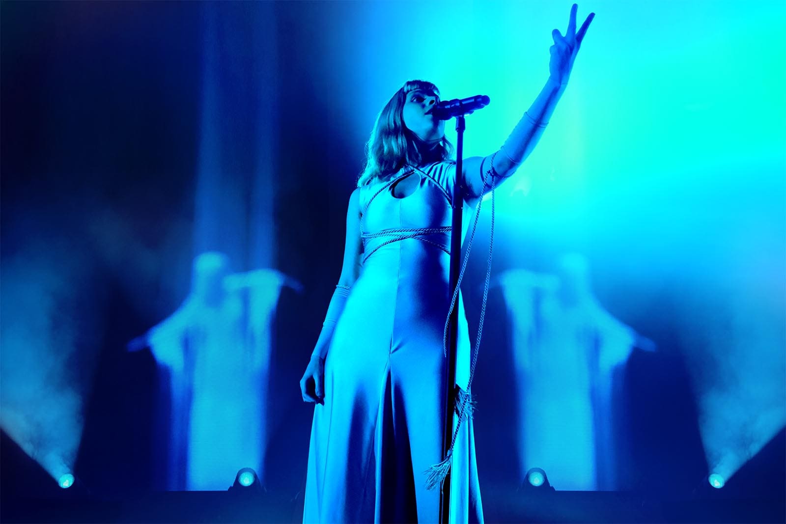 Musician Aurora onstage wearing a jumpsuit, bathed in blue light.