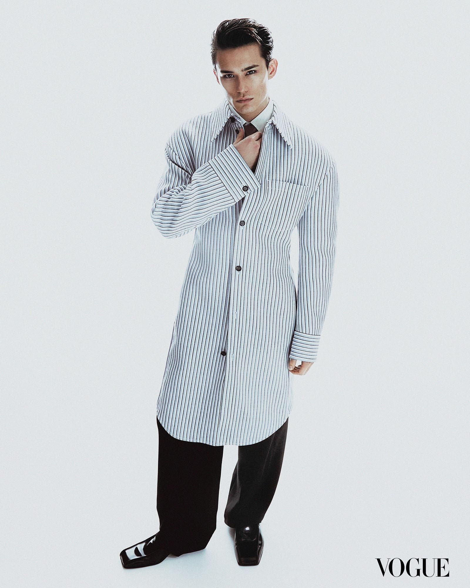 A full-body shot of Alex Schlab wearing an oversized button-down, black slacks, and polished shoes.