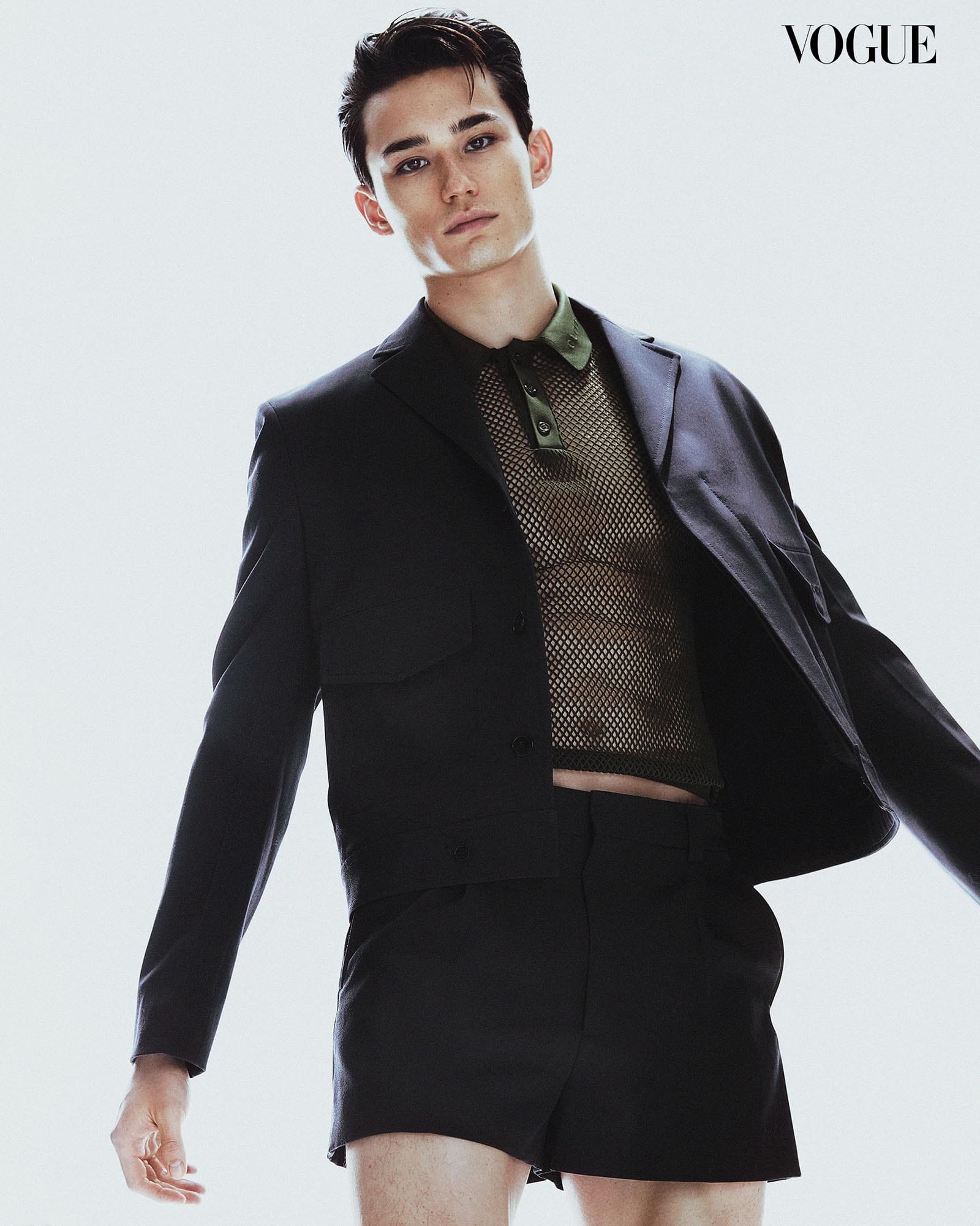 Alex Schlab wears a dark suit jacket and shorts with an army green mesh polo shirt underneath.