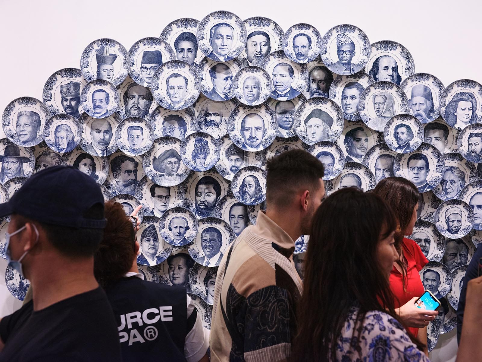 Bon Appetit II by Carlos Aires is a work of art involving porcelain plates with faces of prominent figures printed on them.