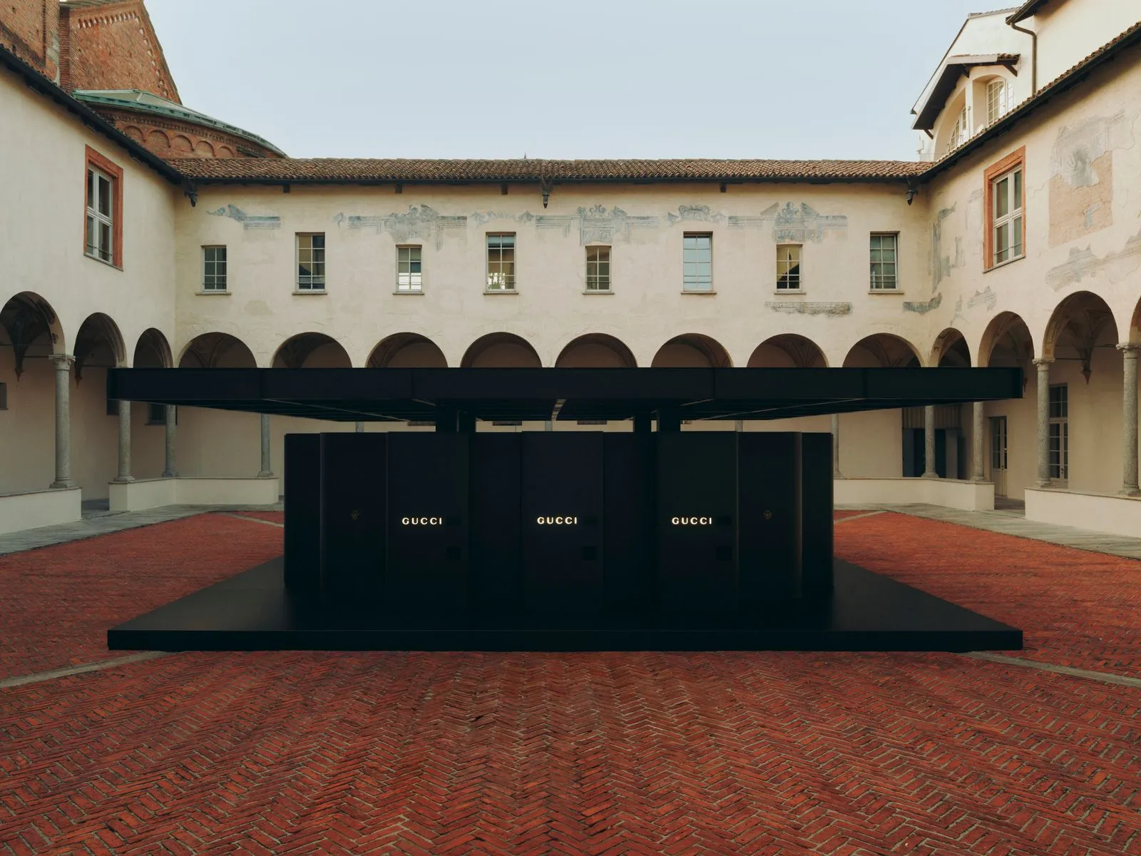Black Gucci product display with illuminated Gucci logos in an open courtyard with arches and brick flooring
