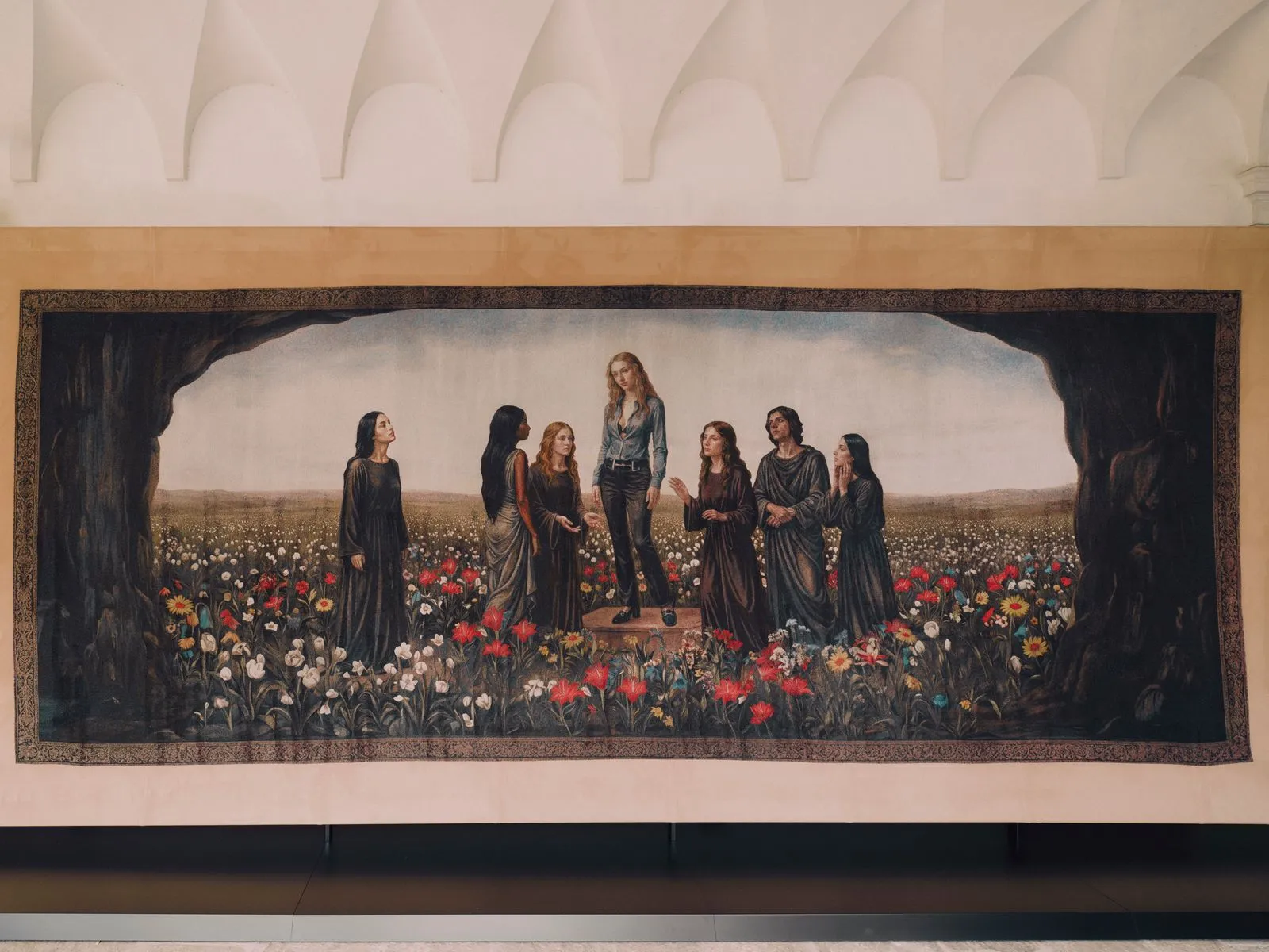 A taller woman stands on a pedestal surrounded by robed figures in a field of colorful flowers, framed by a dark cave-like border.