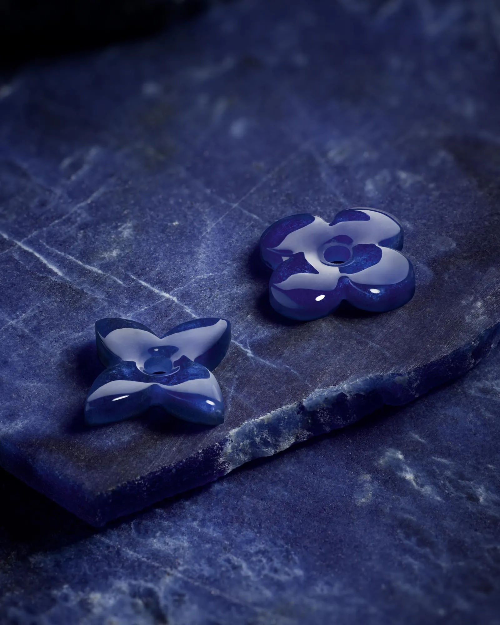 Blue glass flower-shaped ornaments arranged on a dark, textured stone surface.