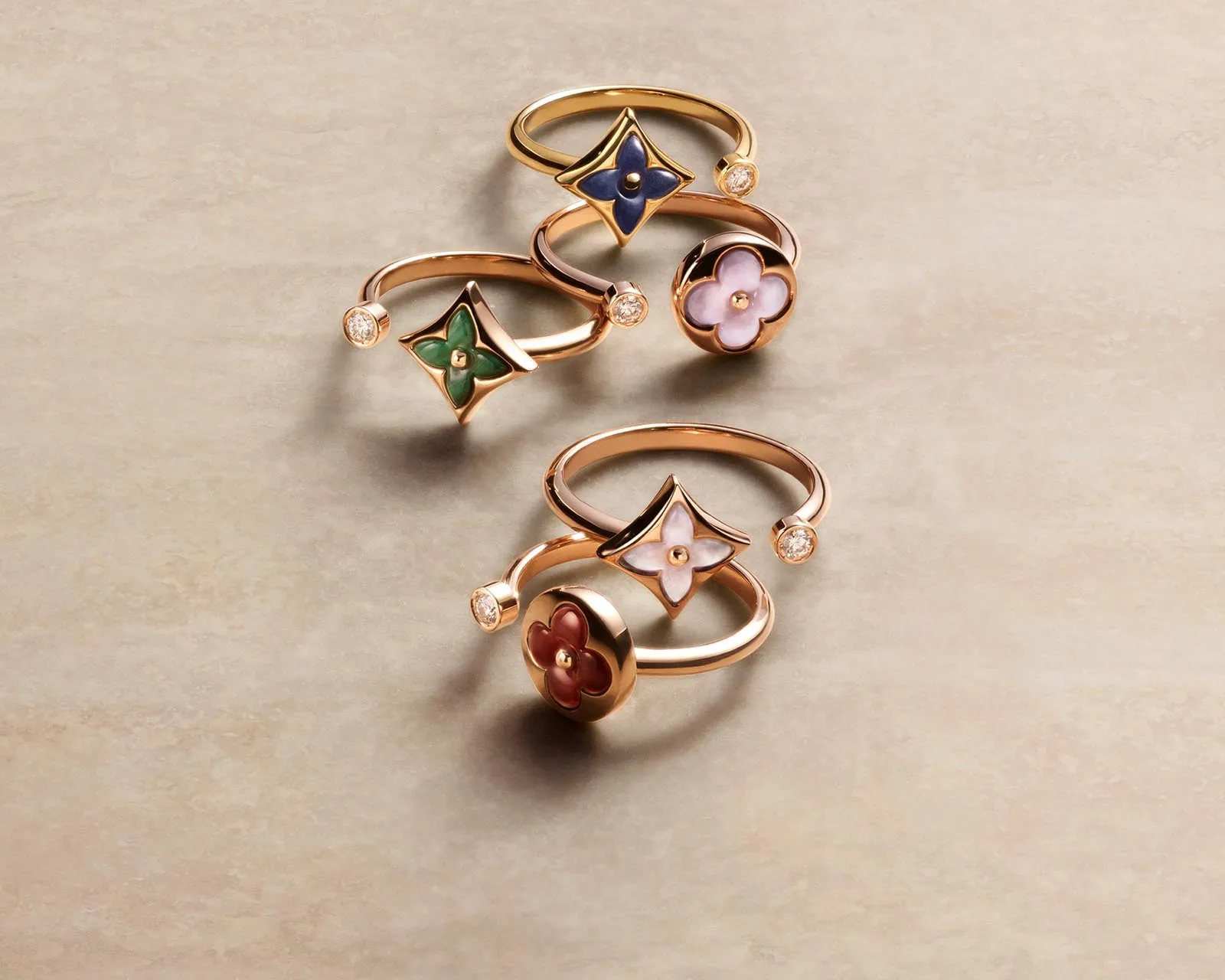 Rose-gold rings with enamel flower motifs in green, blue, and pink, each accented by small gems.