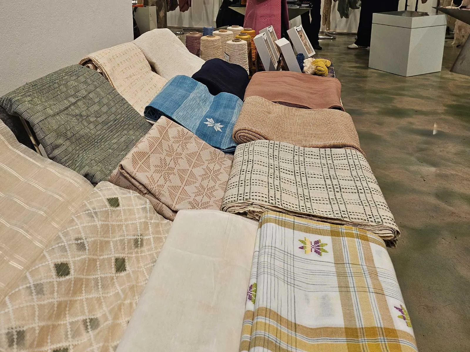 Stacks of folded woven blankets in neutral and pastel colors on a display table in a shop showroom.