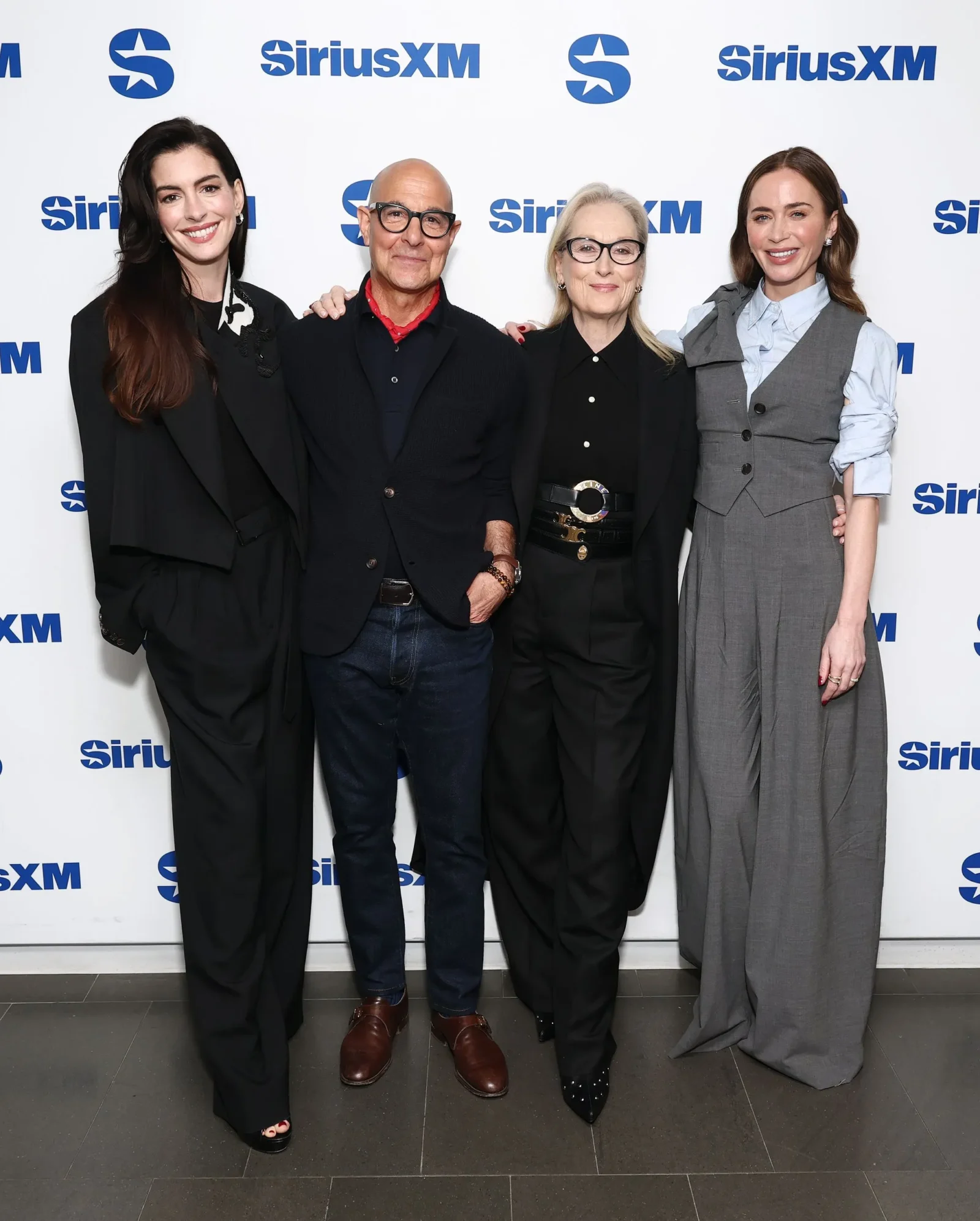 Group of four adults posing and smiling at a SiriusXM event in front of a white backdrop with SiriusXM logos.