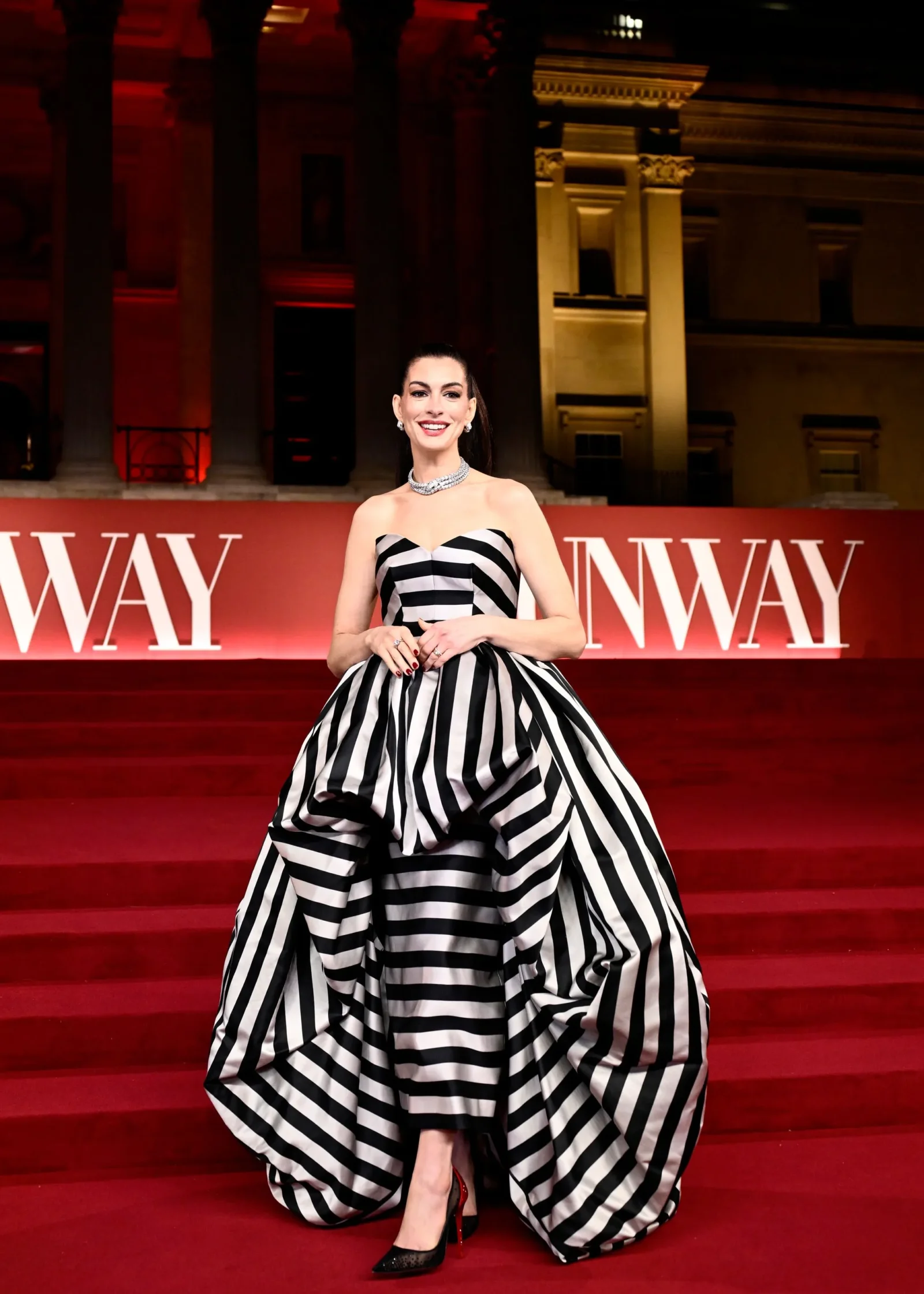 Woman on a red carpet posing in a black-and-white striped strapless ball gown with diamonds at a formal event.