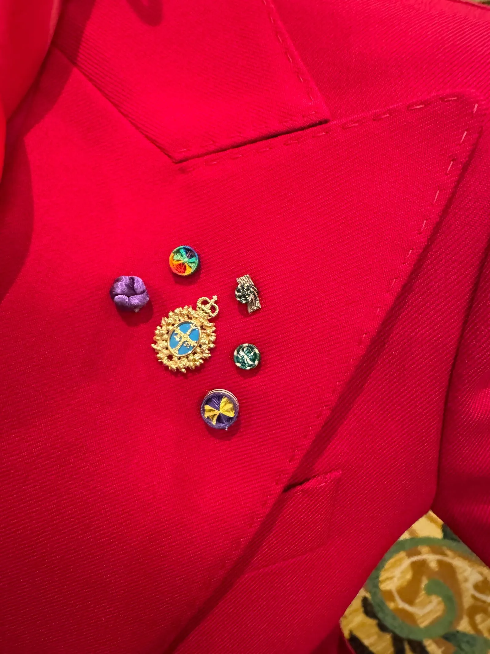 Red blazer adorned with small decorative pins and brooches near the lapel.