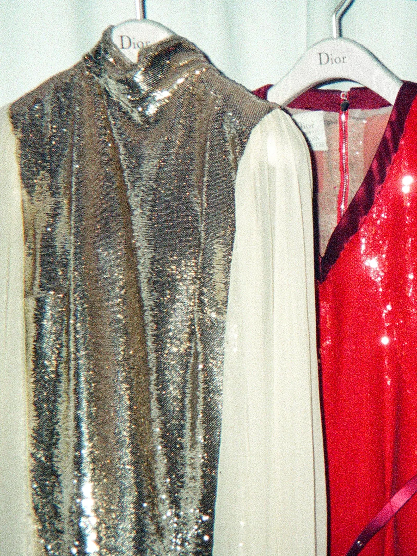 Three Dior dresses on hangers: a silver-sequined gown, a white-sleeved dress, and a red sequin gown on a clothing rack.
