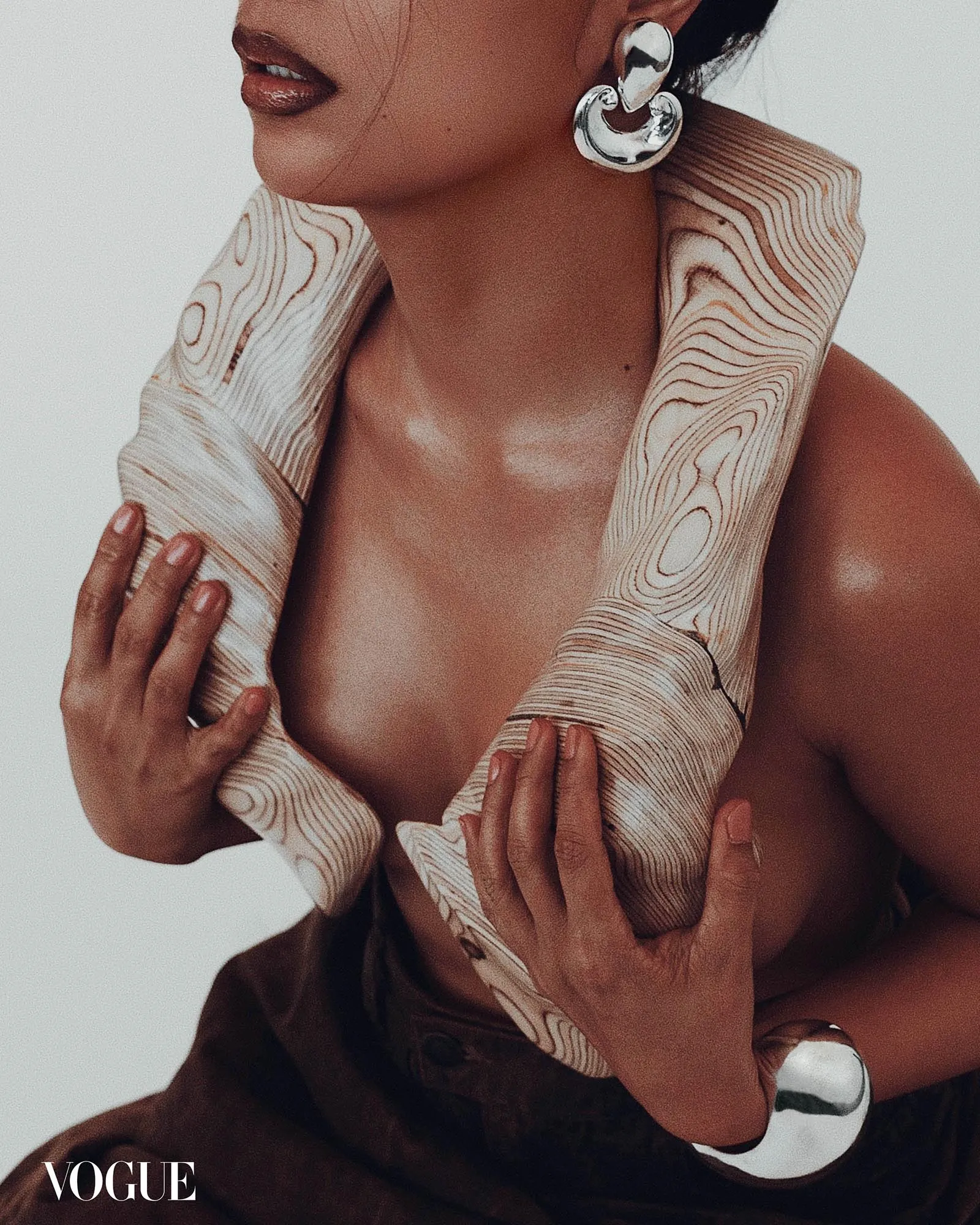 Close-up of a model's neck and lips with a patterned scarf wrapped around, large silver earrings, Vogue watermark.