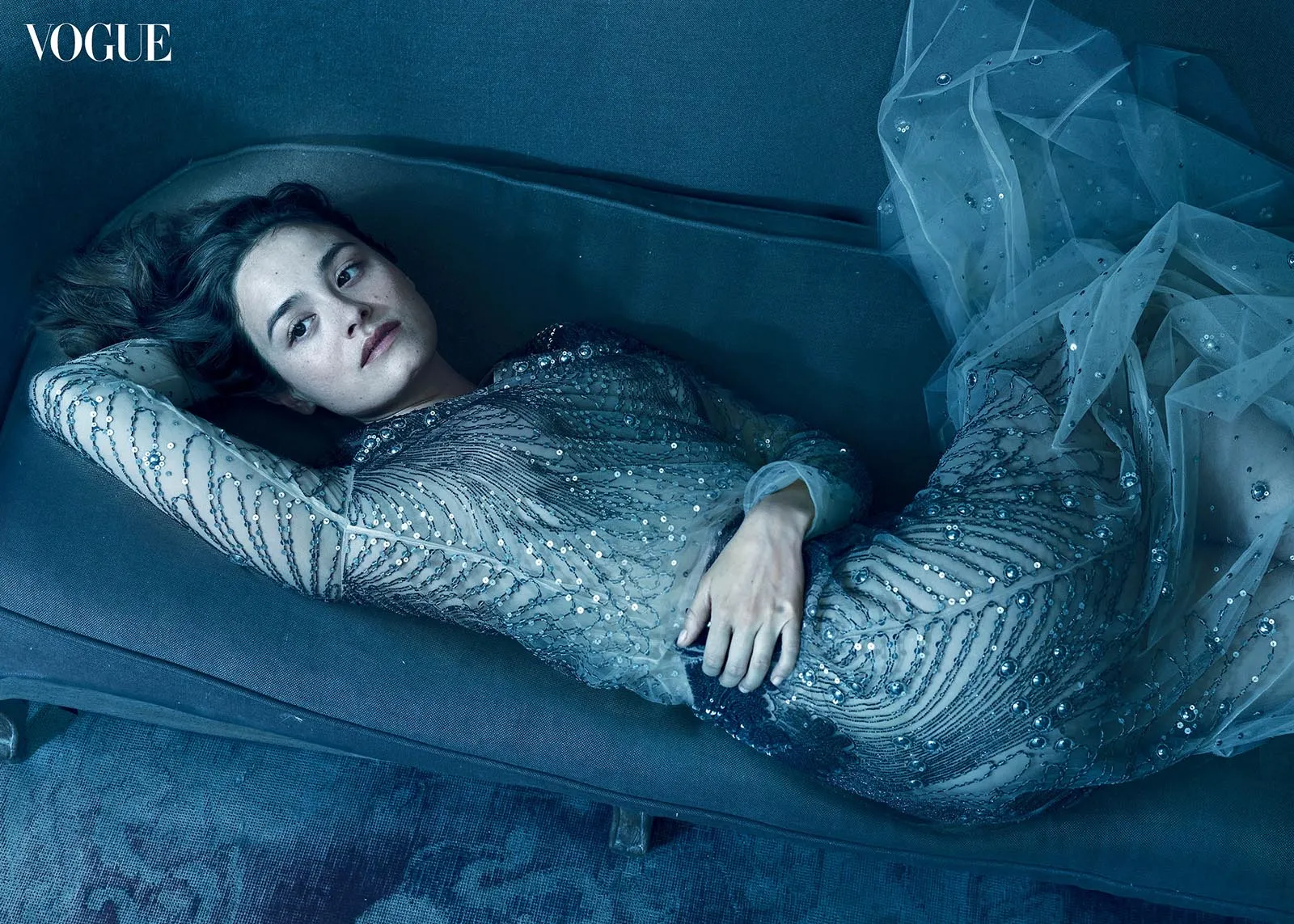 Actor Chase Sui Wonders in a sparkling blue beaded gown lying on a blue sofa; Vogue logo in the top-left.