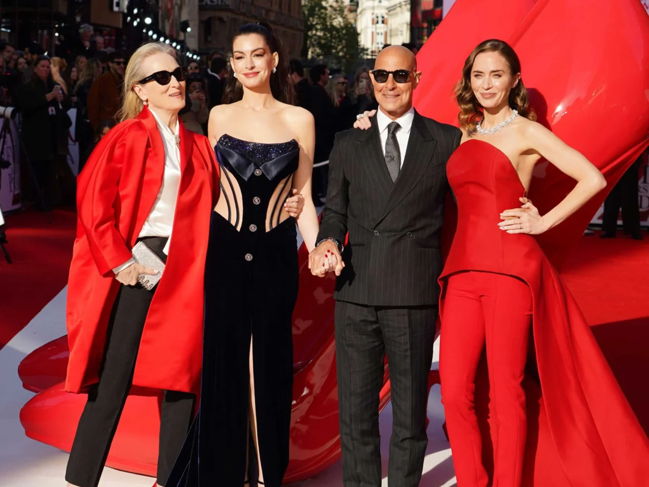 Group of four posing on a red carpet in formal gowns and a suit, photographers in background