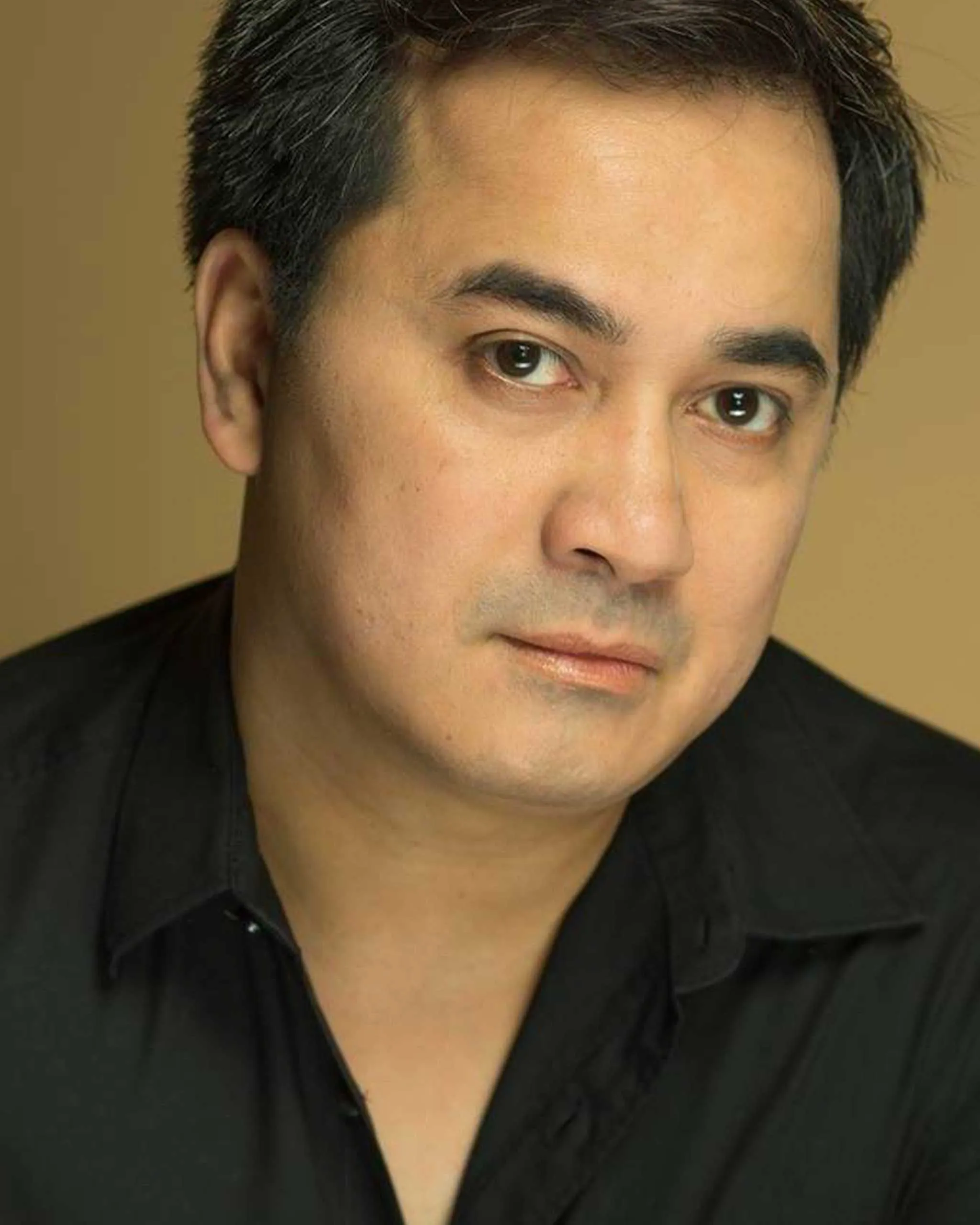 Close-up portrait of a man with dark hair wearing a black shirt, looking slightly to the right.