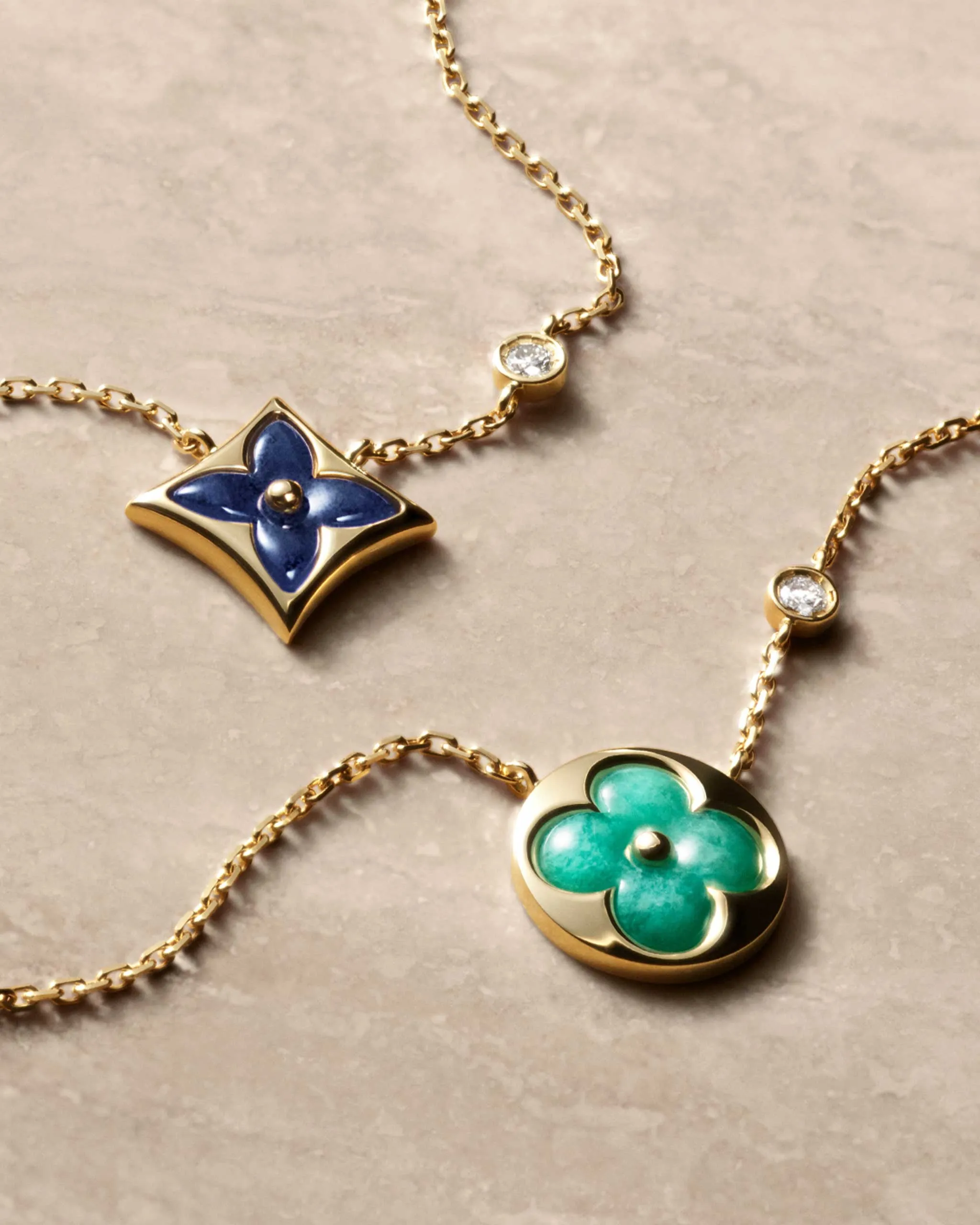 Gold chain necklace with a blue enamel four-leaf-clover pendant against a beige background and a small diamond charm nearby.