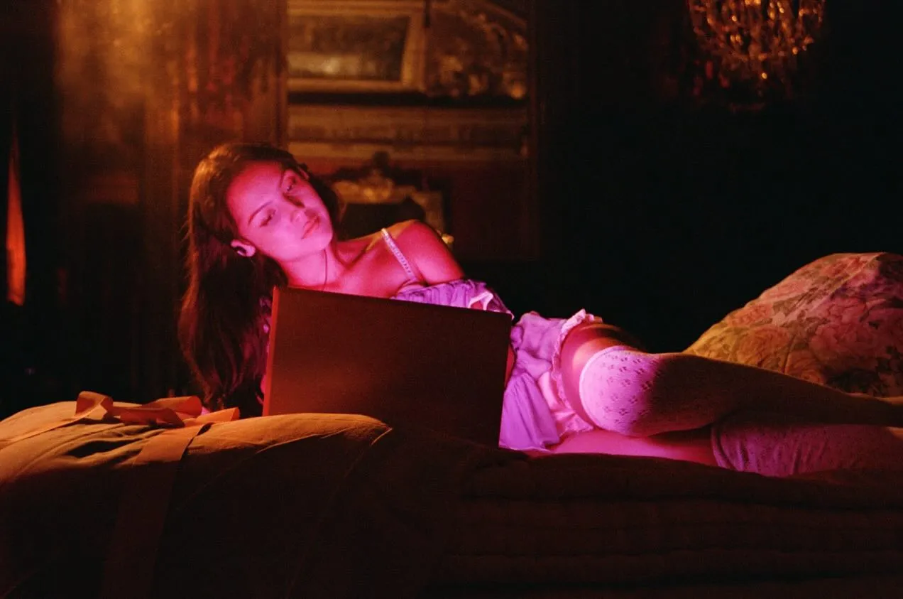 Woman lying on a bed with a laptop, bathed in pink moody light.