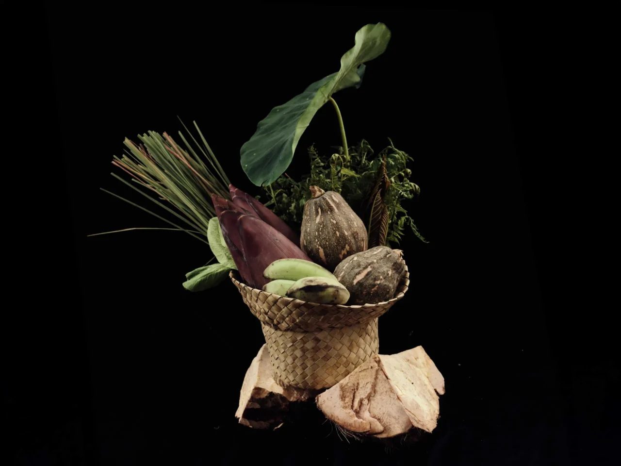 Older woman wearing a sun hat holds a basket of fresh vegetables in a garden.