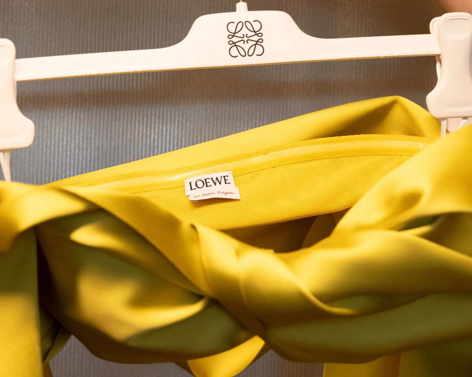 Bright yellow garment on a white Loewe hanger with the logo visible at the top surface of the hanger, against a gray background.