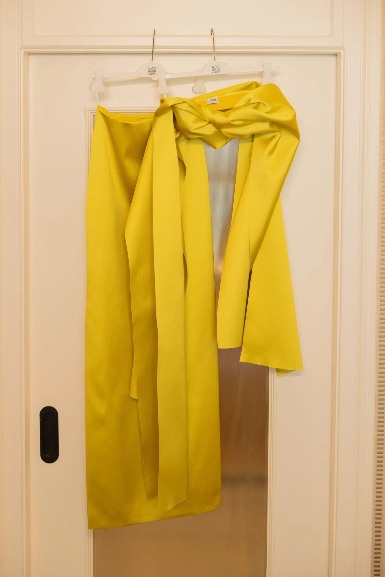 Bright yellow coat hanging on a white hanger over a closet door, Loewe label visible.