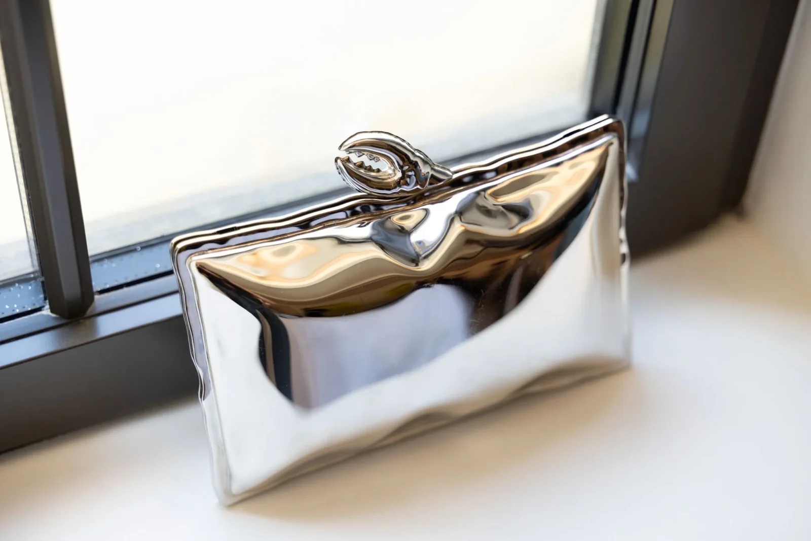 Close-up of a highly polished chrome decorative object resting on a windowsill, reflecting surrounding light and colors.