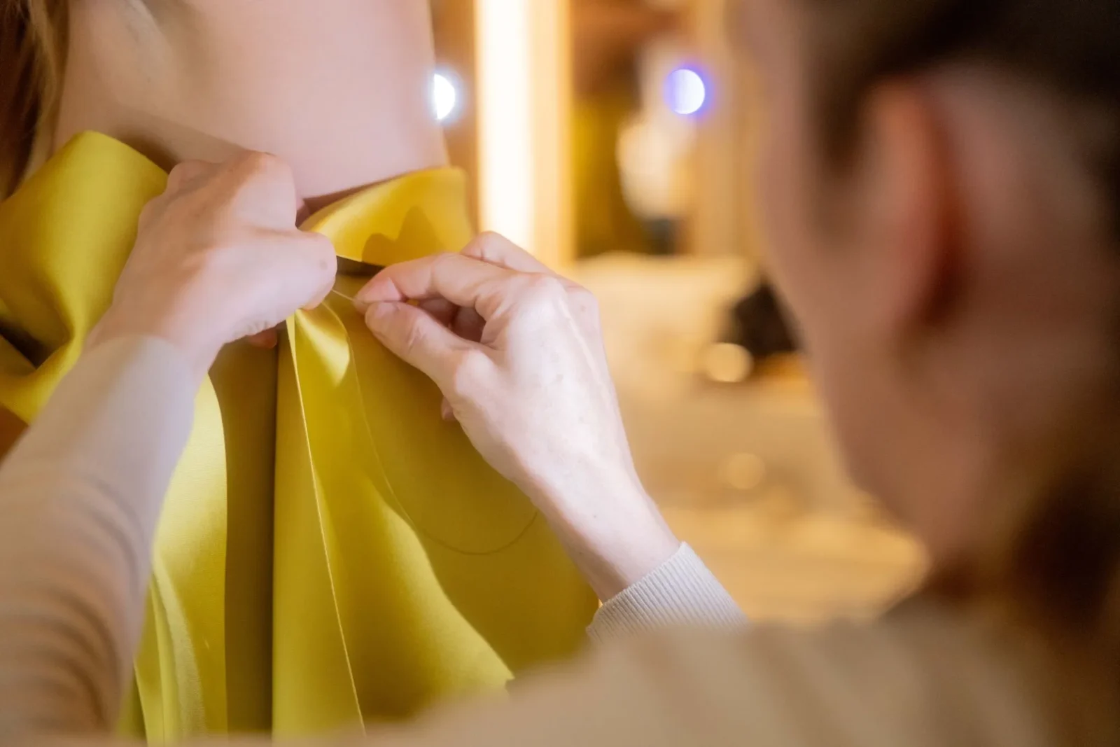 Close-up of hands tying a bright yellow bow around the neck of a yellow garment.