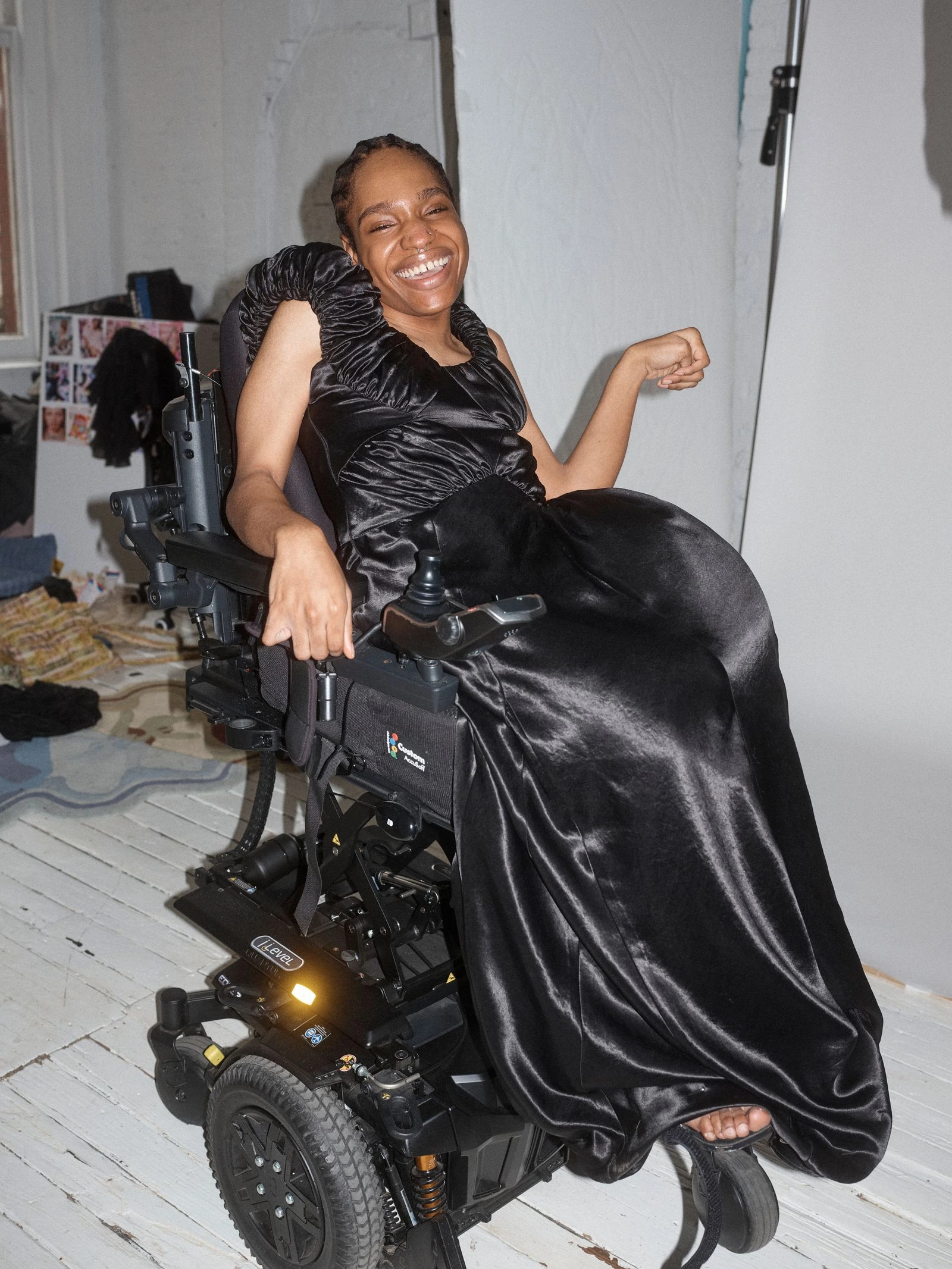 Joyful woman in a black satin gown smiling while seated in a motorized wheelchair in a studio setting