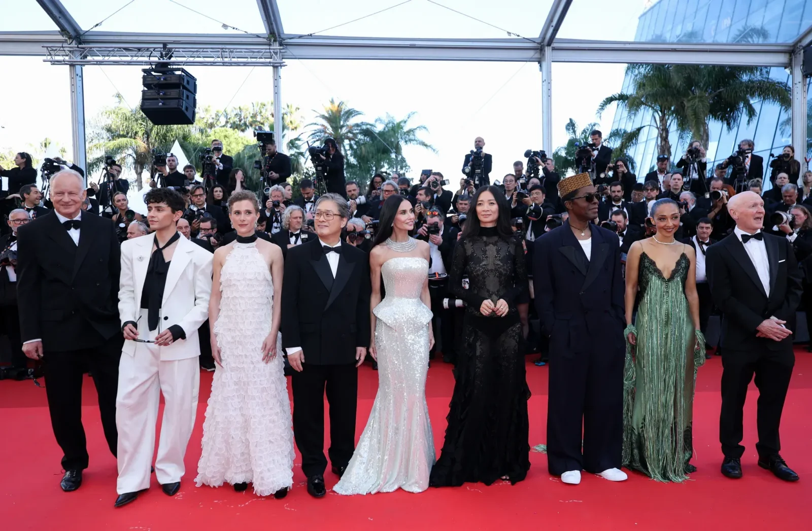 Celebrities posing on a red carpet with cameras flashing from a crowd of photographers in the background.