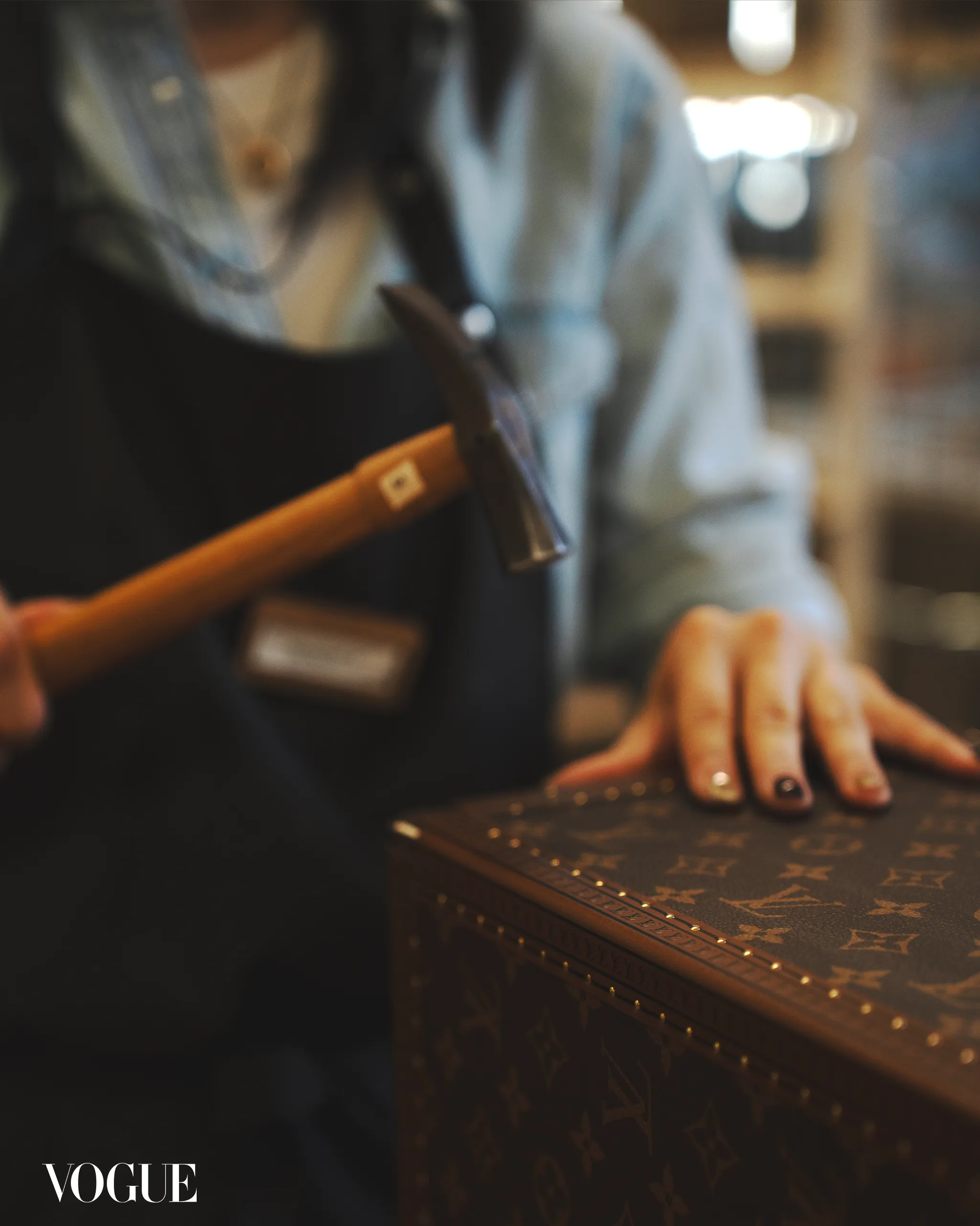 Blurry fashion shot: a person’s hand rests on a brown, patterned surface with the Vogue logo in the bottom-left corner.
