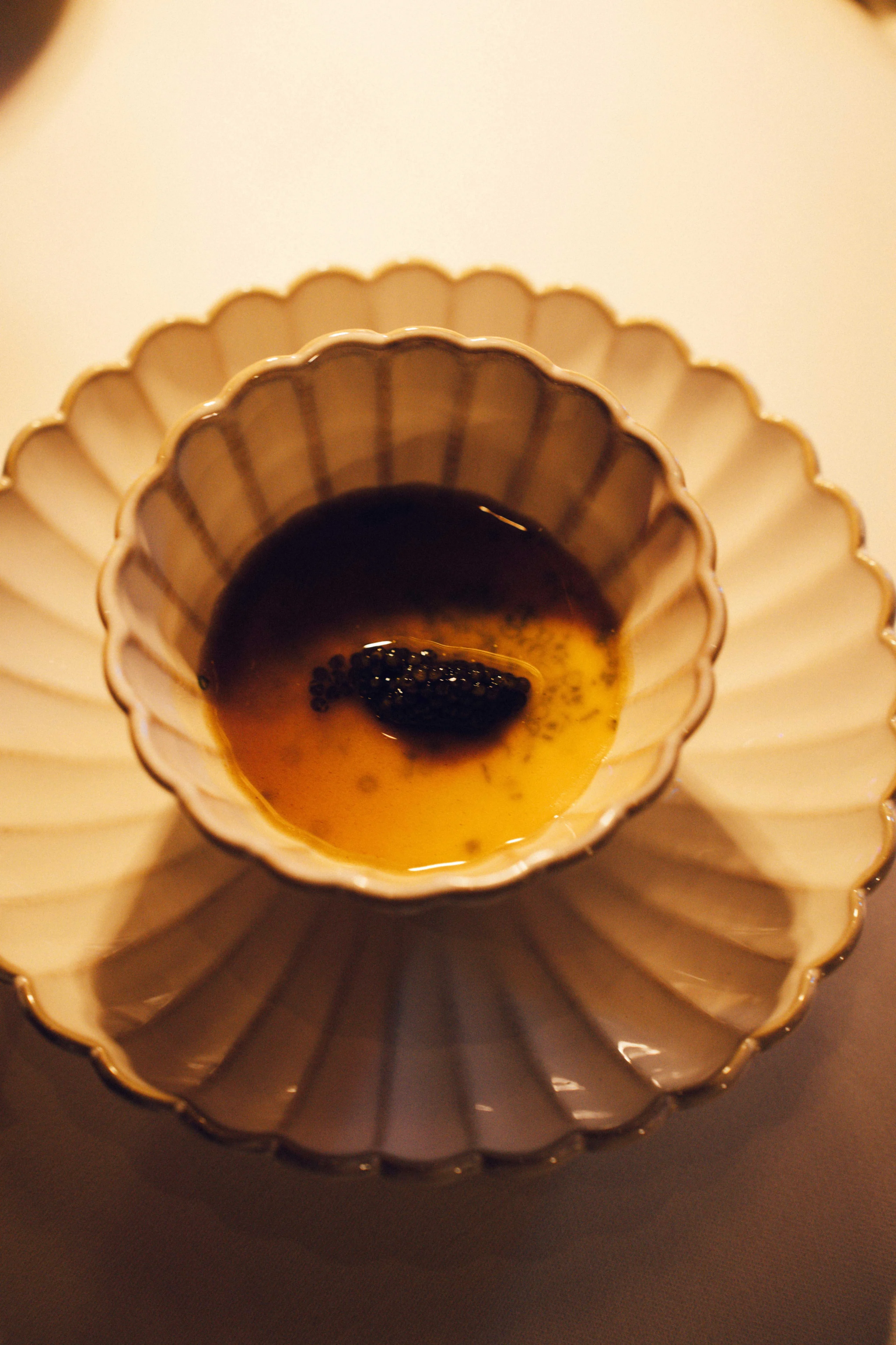 Close-up of a custard cup with black caviar garnish on a scalloped plate.
