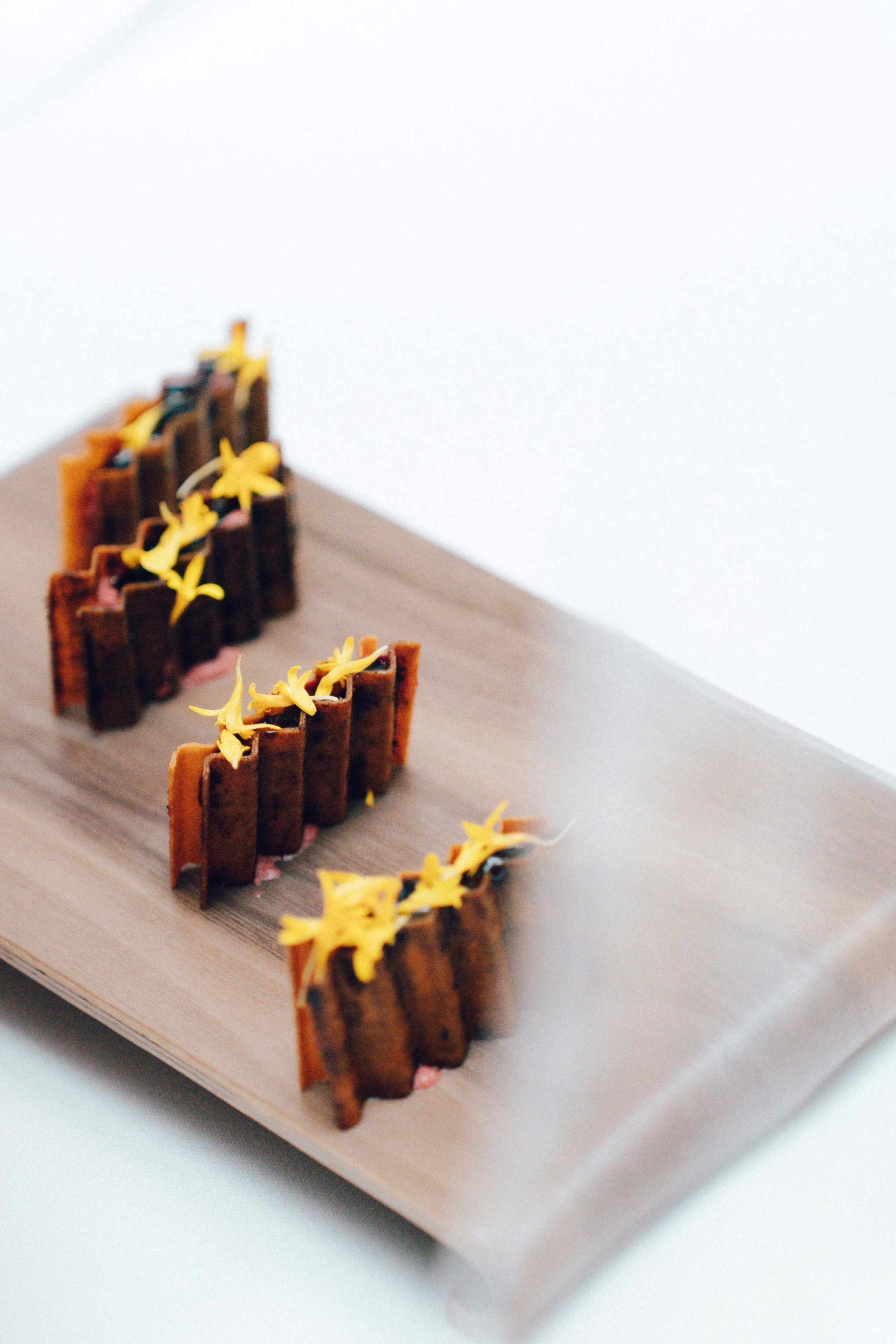 Row of chocolate wafer sticks with yellow flower garnish arranged on a wooden board as a dessert centerpiece