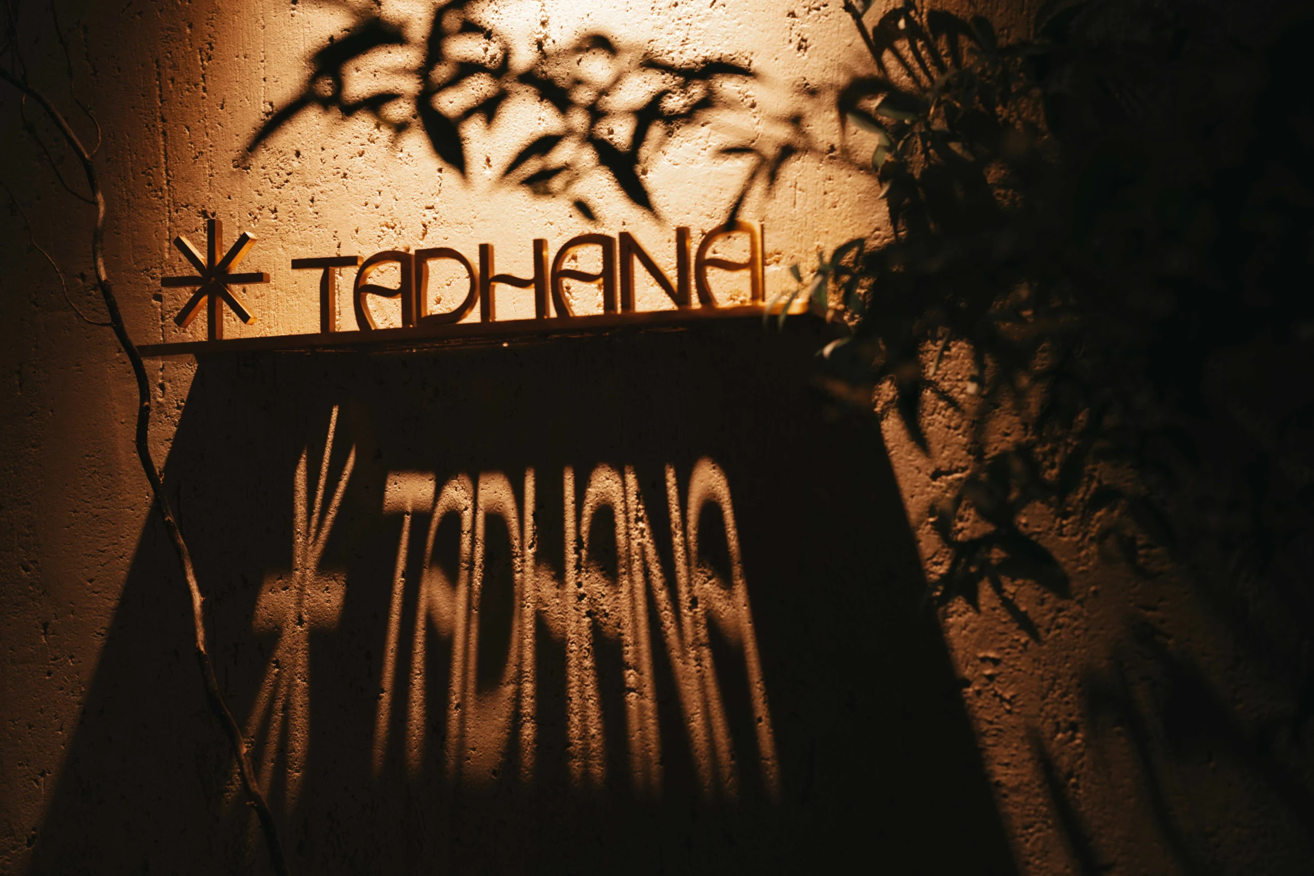 Orange-lit textured wall featuring graffiti with a starburst asterisk and stylized letters.