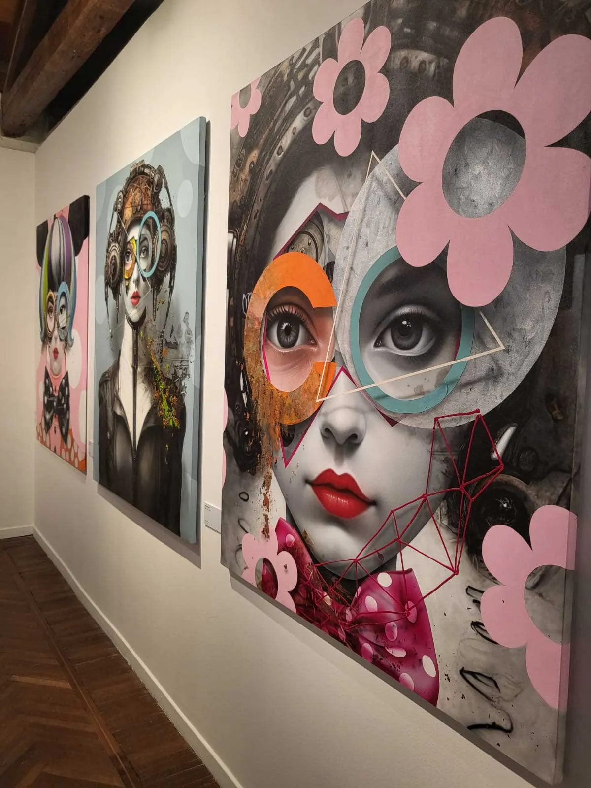 Three large contemporary portraits in a gallery wall, using collage and geometric shapes with pink flower motifs against grayscale faces and bold color accents.