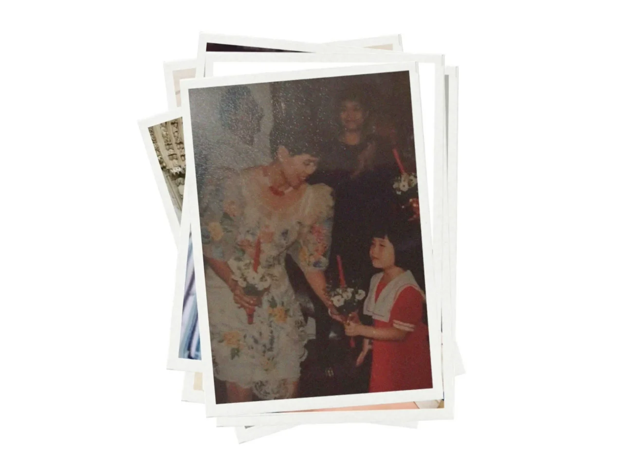 Stack of printed photos featuring a wedding moment: a bride in a floral white dress receives flowers from a guest in red.