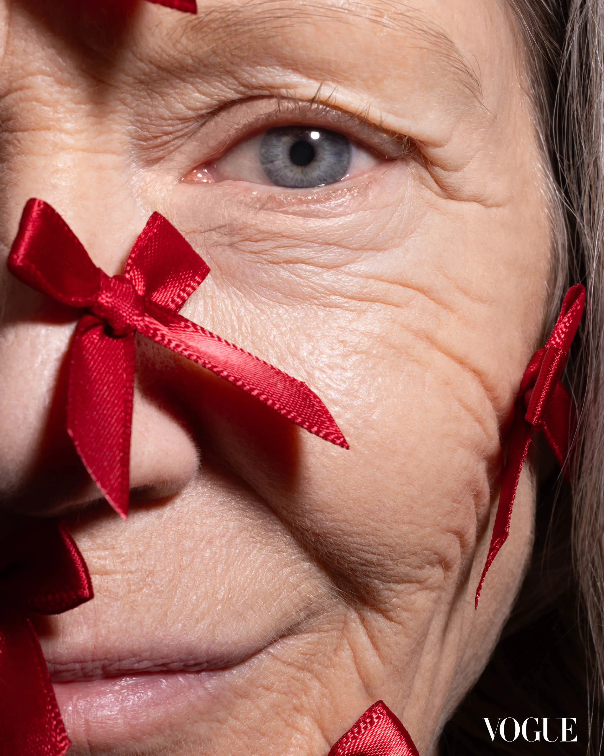 Close-up of an elderly woman's blue eye framed by red satin ribbons.