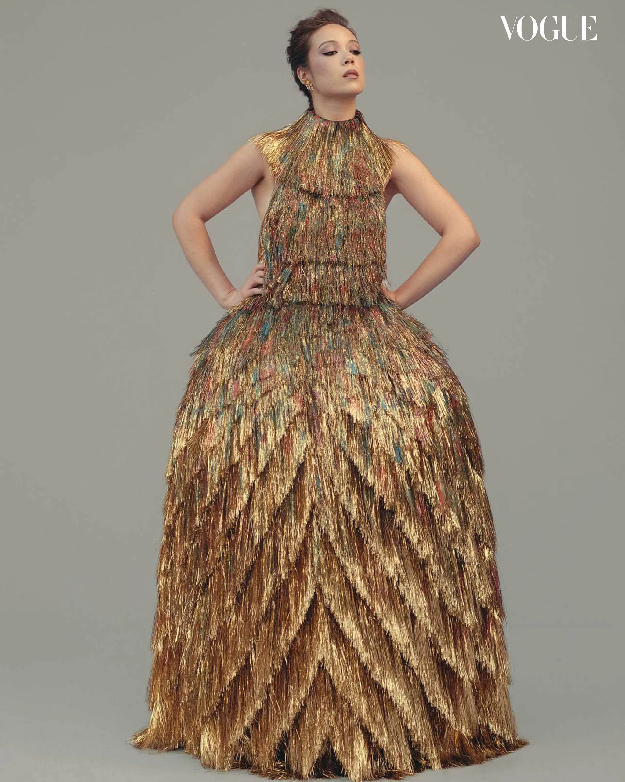 Model in a metallic, multi-colored fringe gown posing with hands on hips for a Vogue fashion shoot.