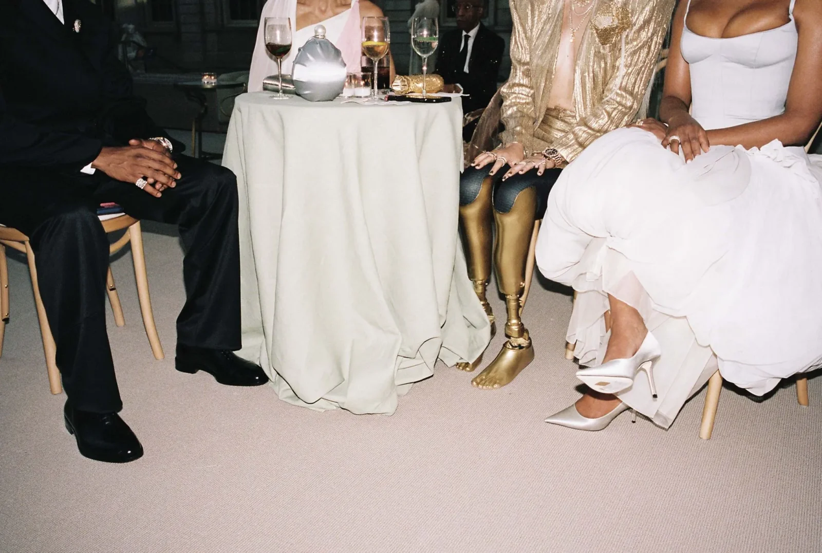 Group of people in formal attire seated around a small round table at a gala; hands resting in laps, drinks on the table nearby