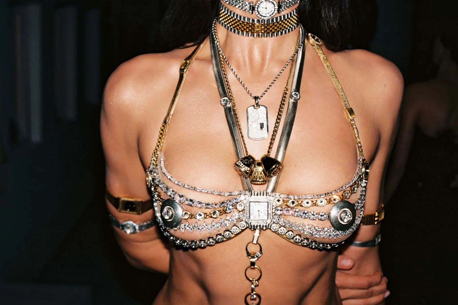 Close-up of a chest adorned with multiple gold and silver necklaces and statement pendants with a bare backdrop.