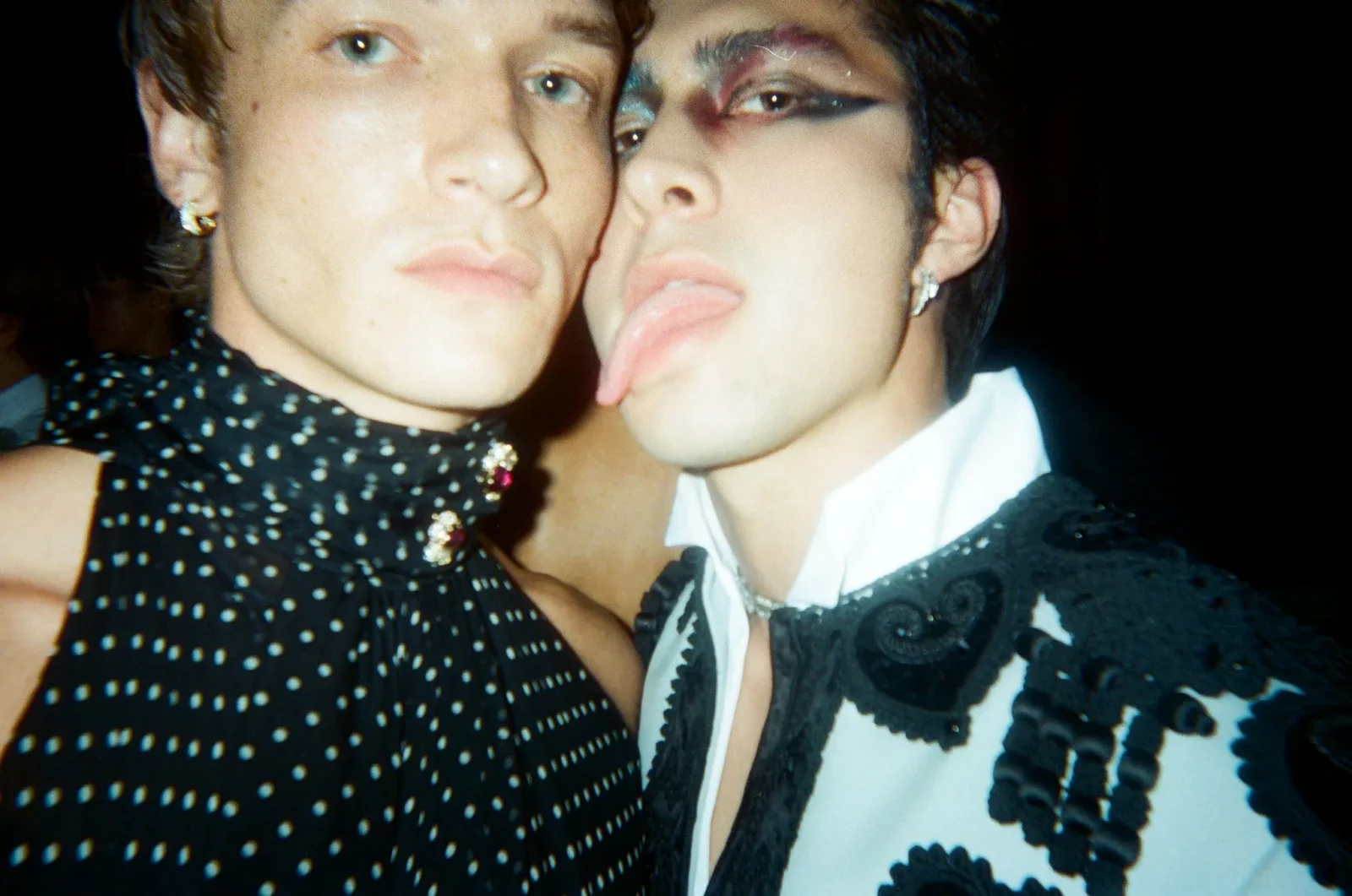 Two people posing closely for a selfie, making pouty lips at the camera against a dark background.