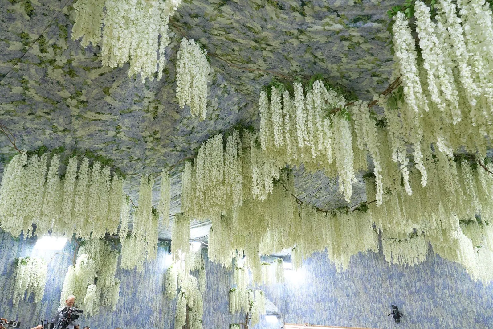 Indoor room with cascading white flowers hanging from the ceiling and along the walls, creating a floral canopy.