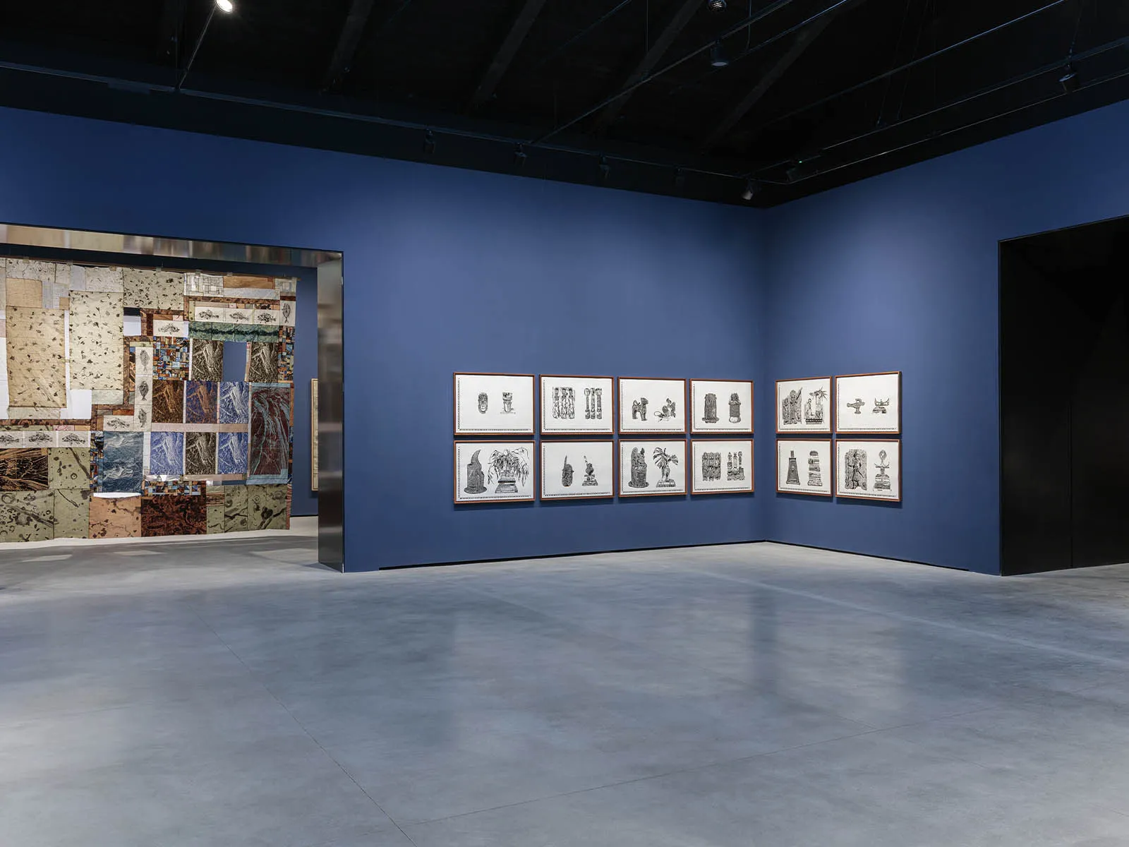 Museum gallery interior with a blue wall showcasing a row of framed black-and-white prints arranged horizontally.