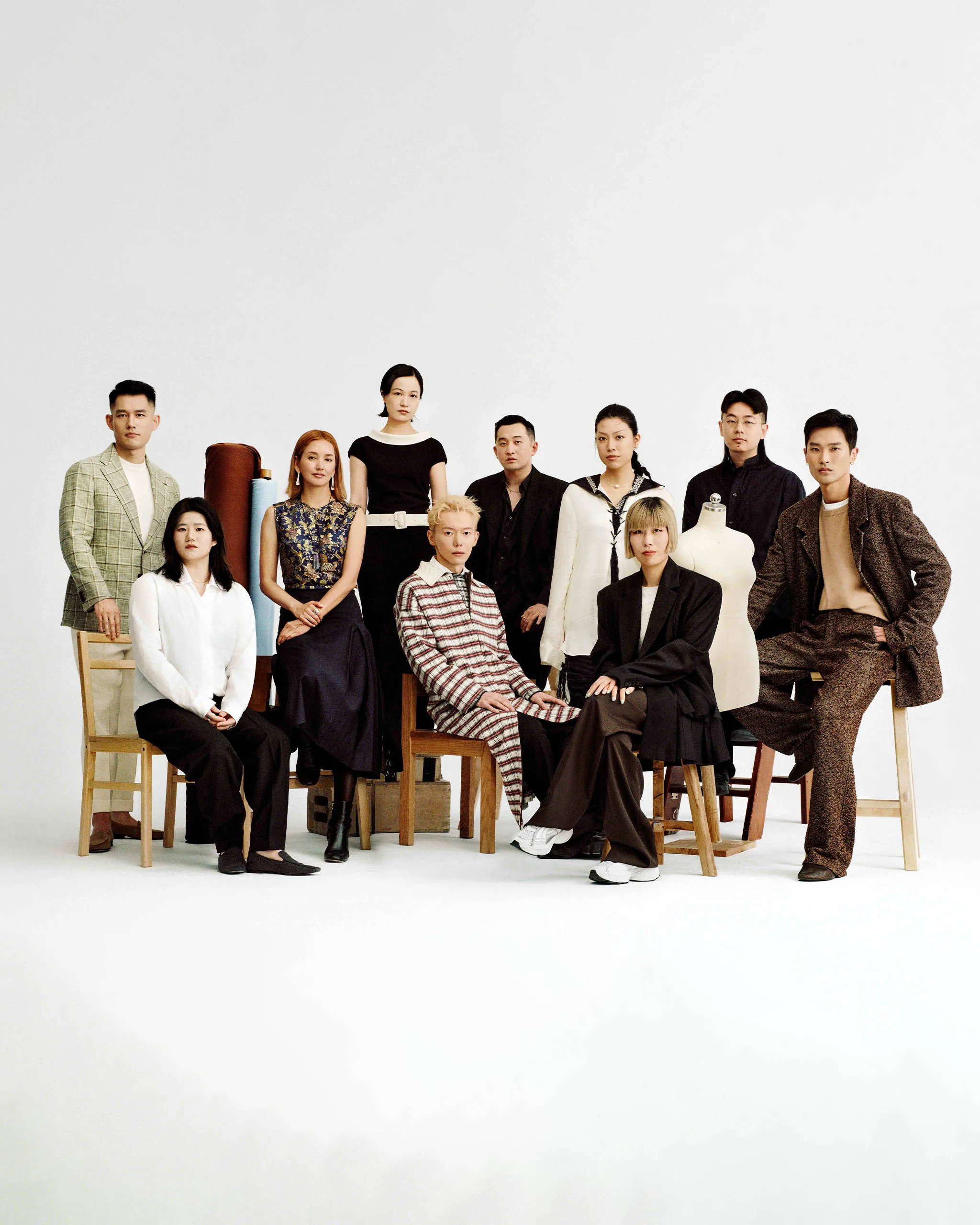 Group of diverse fashion models posing in a studio with dress forms and fabric rolls.