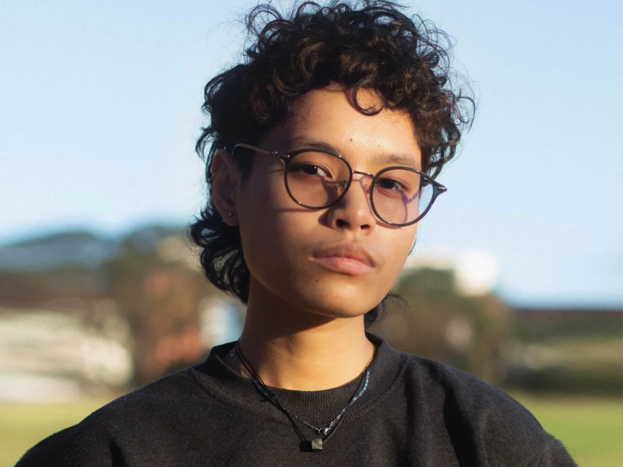 Three portraits side by side of people wearing glasses, each looking at the camera; left has curly hair and denim jacket, center platinum hair, right curly hair.