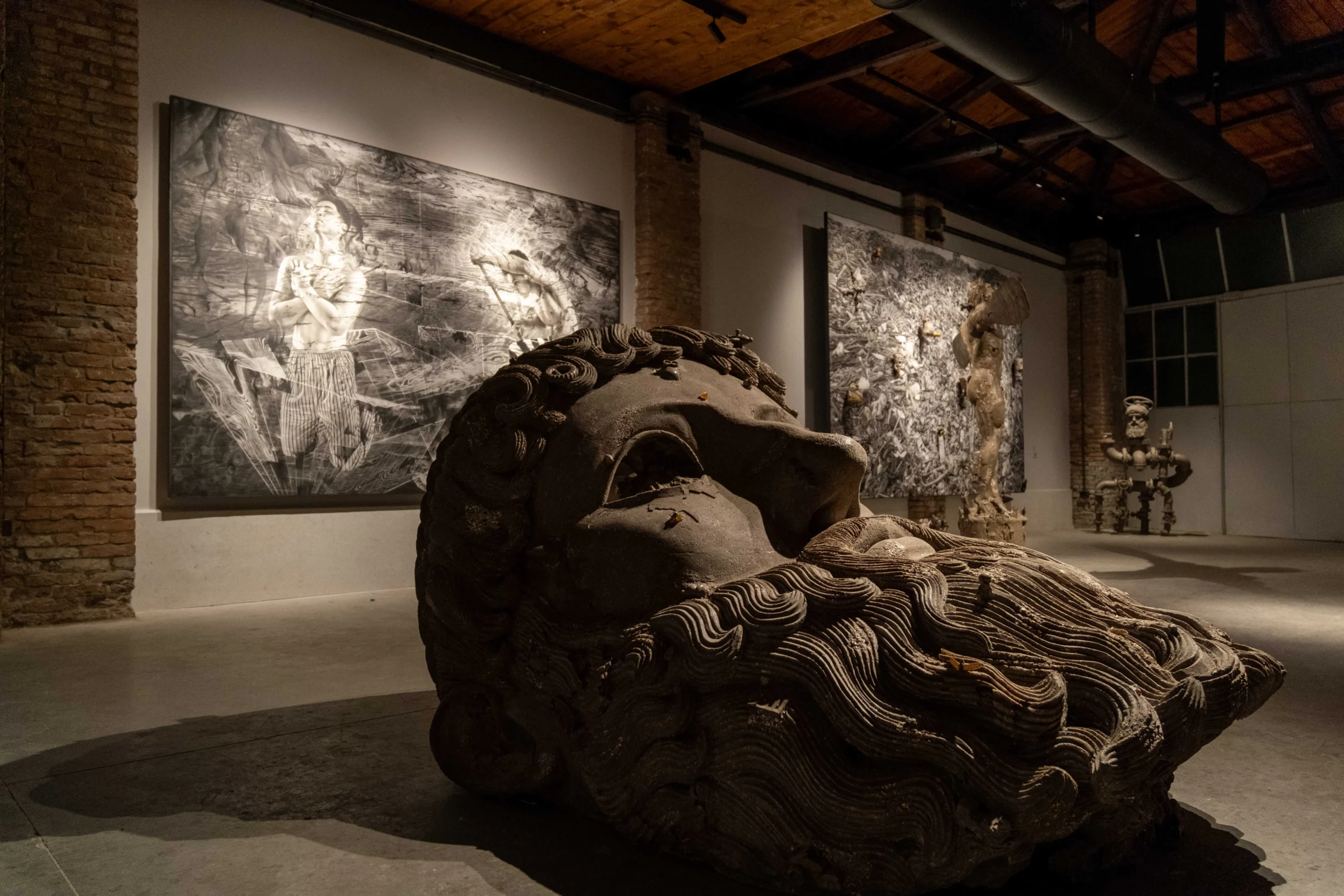 Dimly lit museum gallery with a large textured stone sculpture in the foreground and monochrome wall panels in the background.