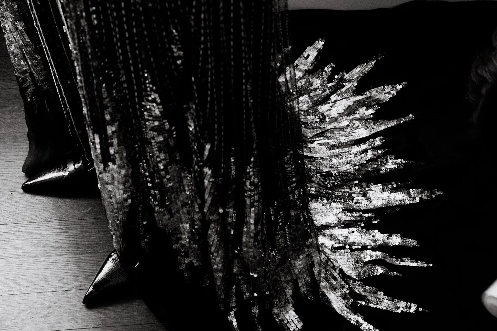 Close-up of black fabric with silver sequins arranged in a fringe pattern on a dark surface.