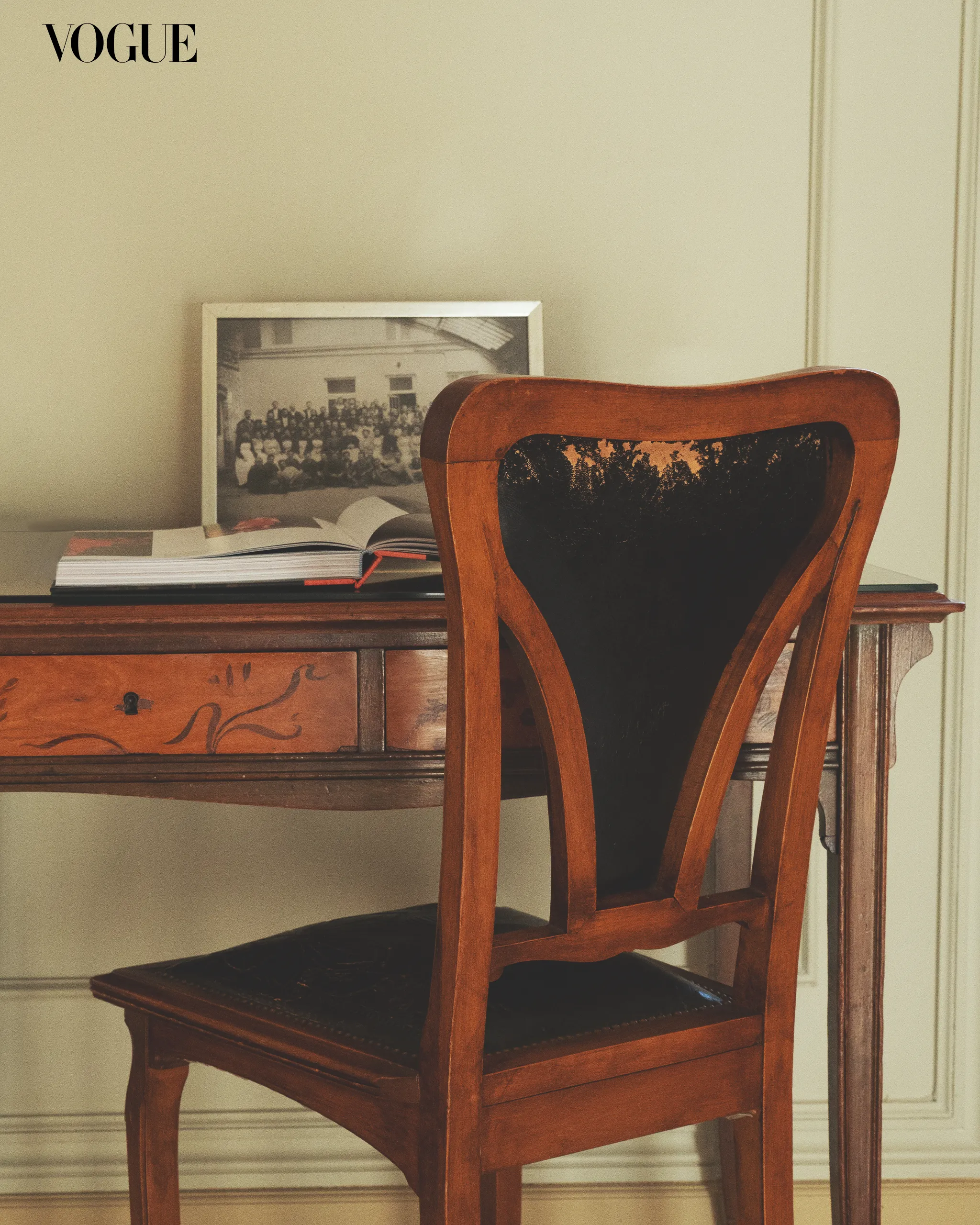 Wooden chair at a desk with a framed black-and-white photo and an open book; Vogue logo in the top-left corner.