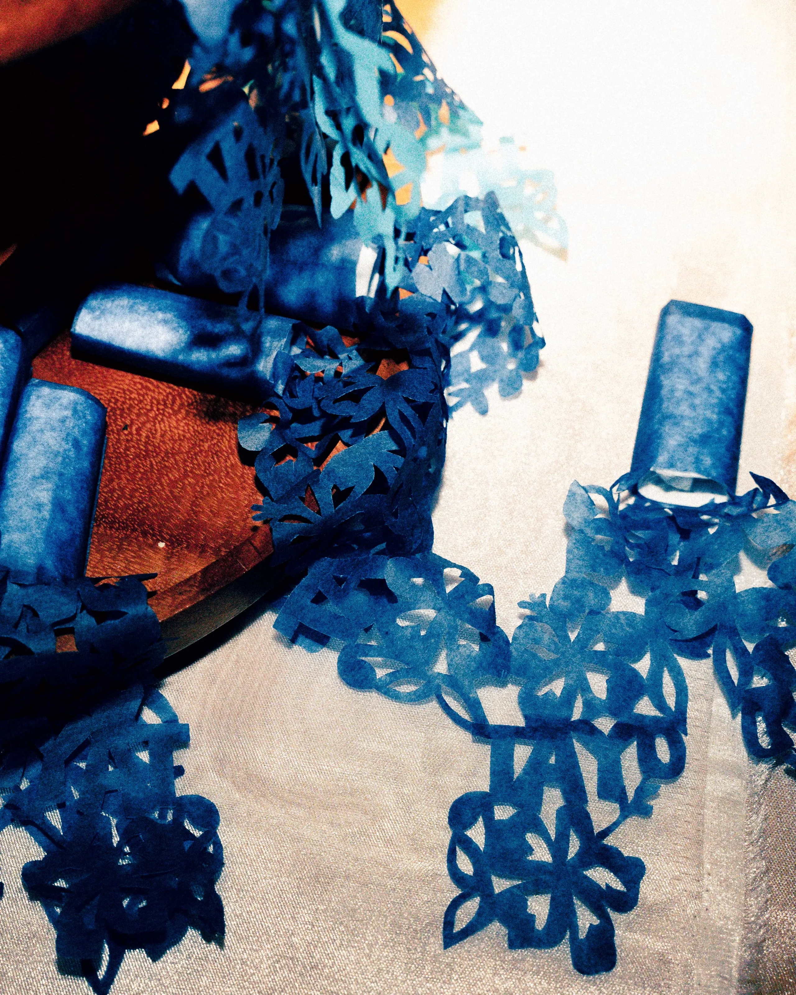 Blue paper cut-out shapes forming a loose chain on a light fabric background.
