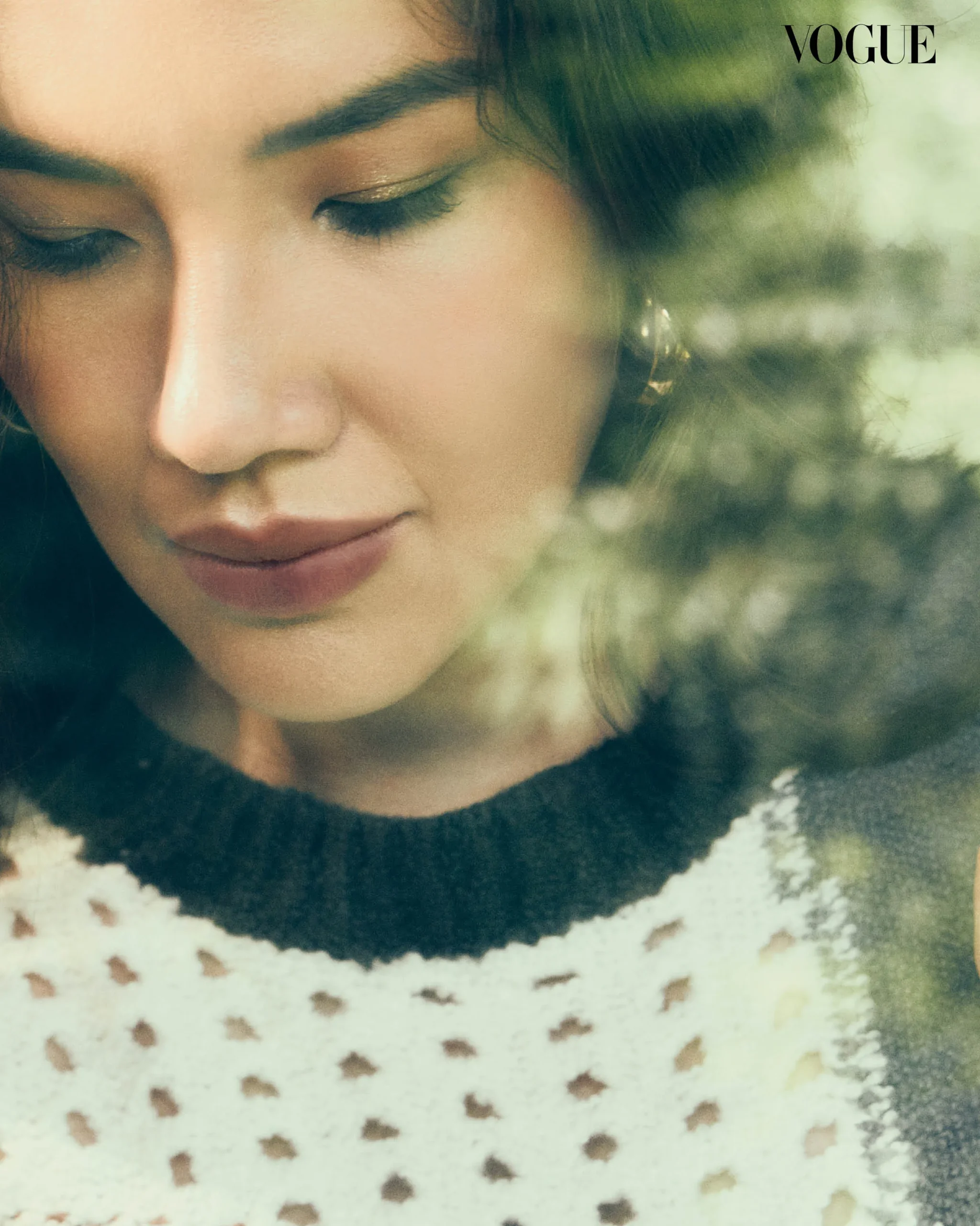 Close-up of a woman's face with eyes closed and soft makeup, wearing a dotted knit; Vogue logo in the corner.