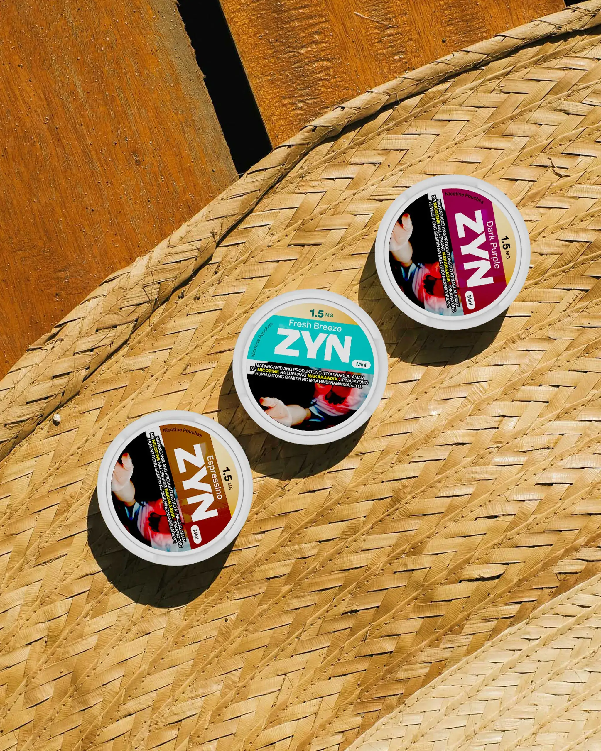 Several ZYN nicotine pouch tins placed on a woven straw surface, showing blue, pink, and brown labels (product shot).
