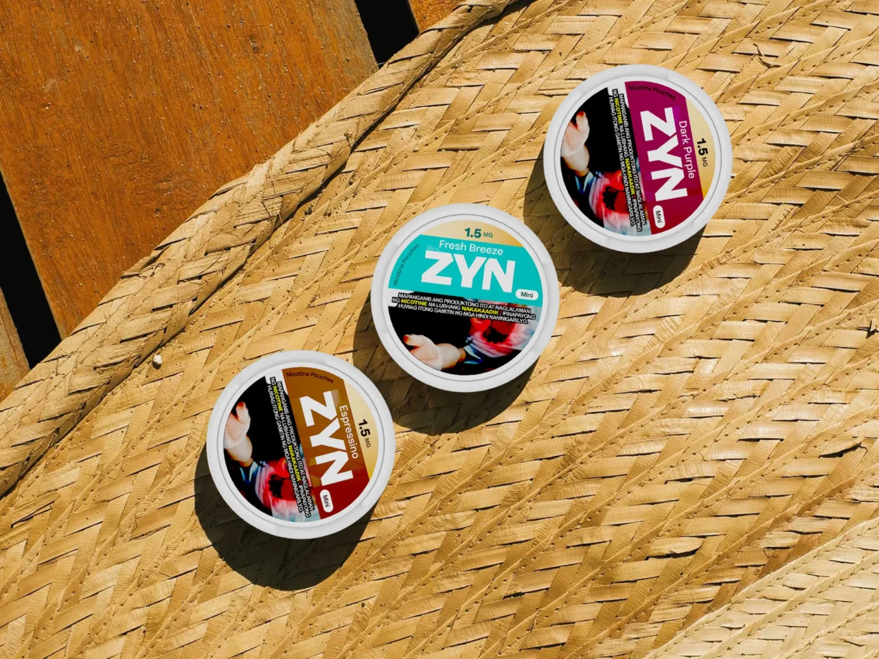 Assorted ZYN nicotine pouch tins resting on a woven straw mat, showcasing different flavors and colors.